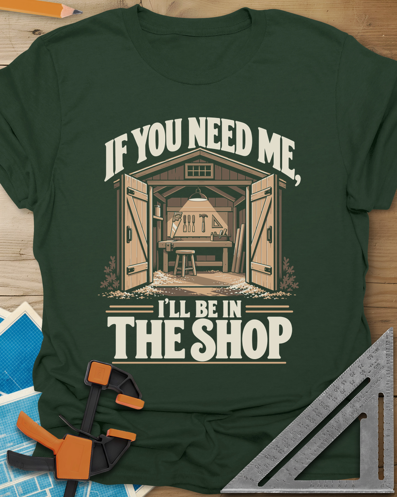 In The Shop t-shirt in Forest Green, a small open workshop with a hanging lamp, bench and wall tools