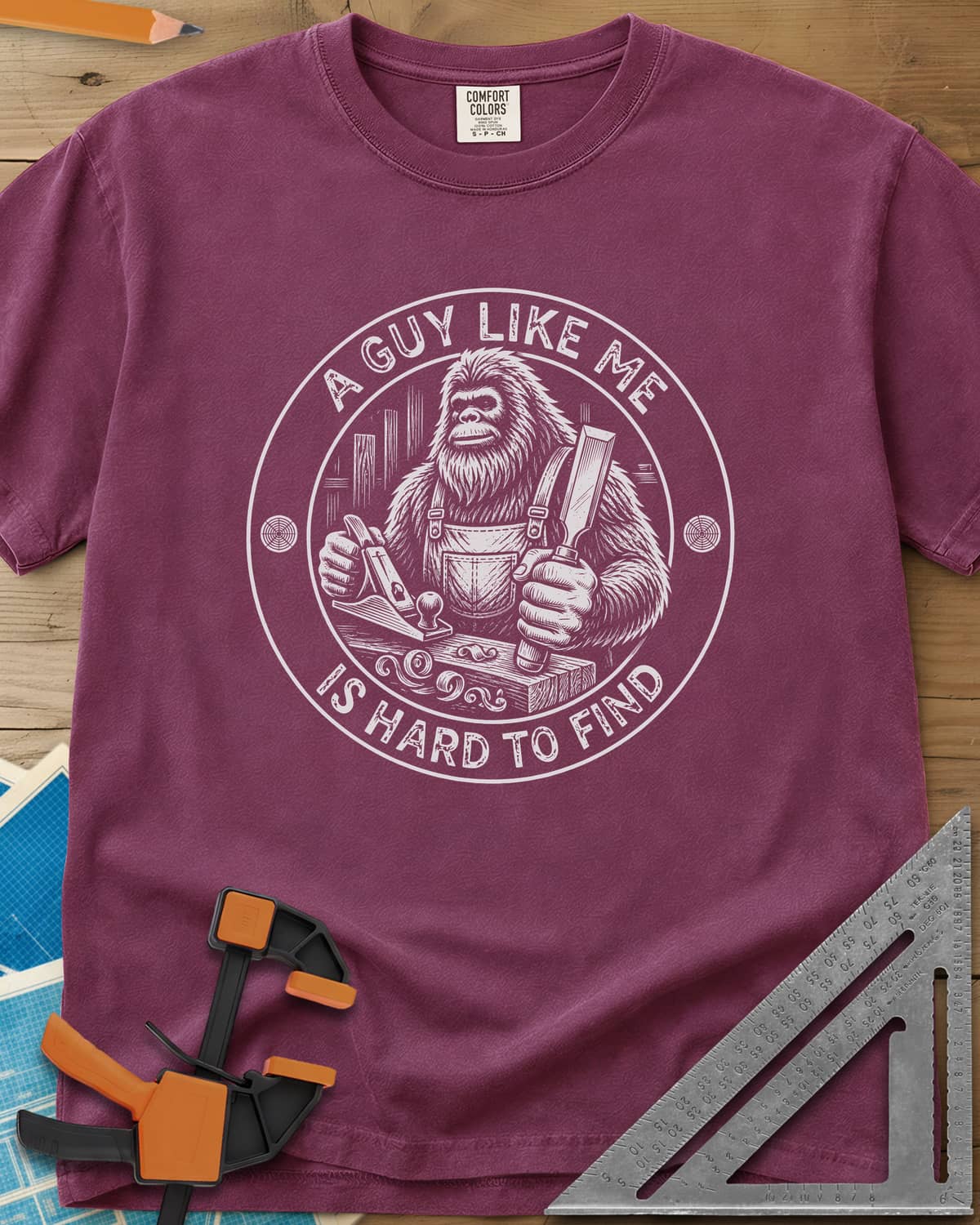 A Guy Like Me Is Hard To Find Woodworking heavyweight tee in Berry, Bigfoot in overalls with a hand plane and chisel inside