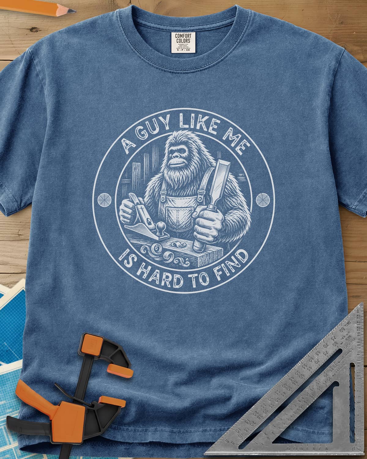 A Guy Like Me Is Hard To Find Woodworking heavyweight tee in Blue Jean, Bigfoot in overalls with a hand plane and chisel