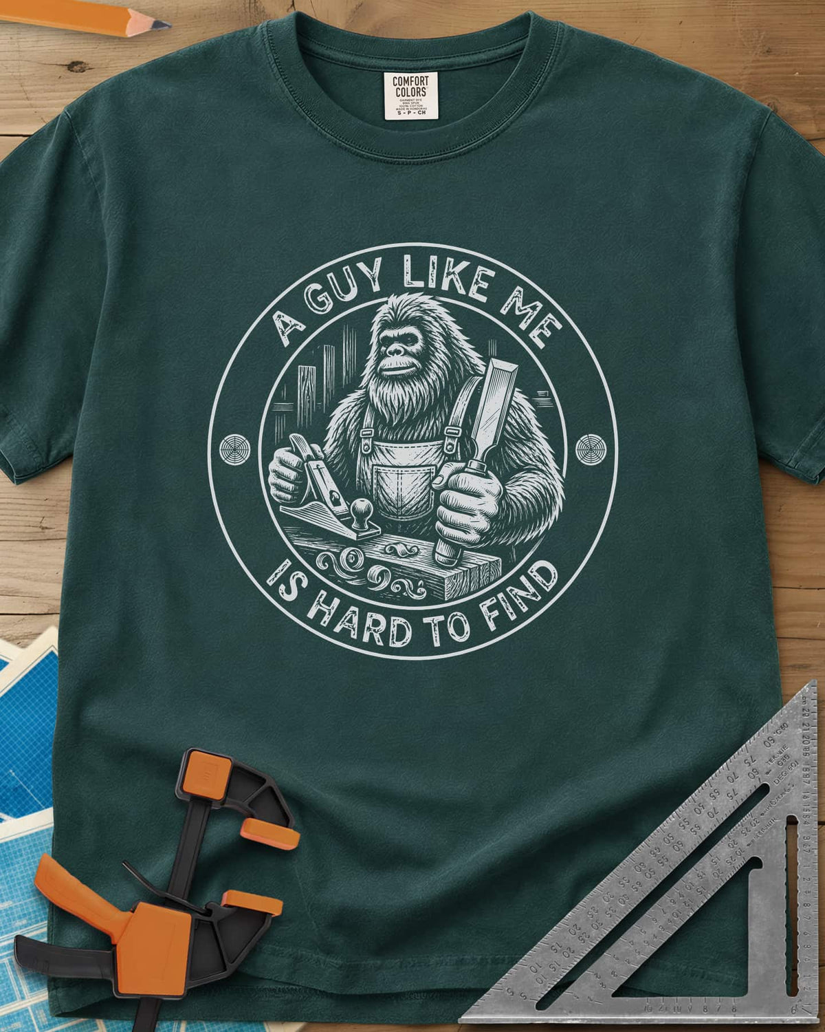 A Guy Like Me Is Hard To Find Woodworking heavyweight tee in Blue Spruce, Bigfoot in overalls with a hand plane and chisel