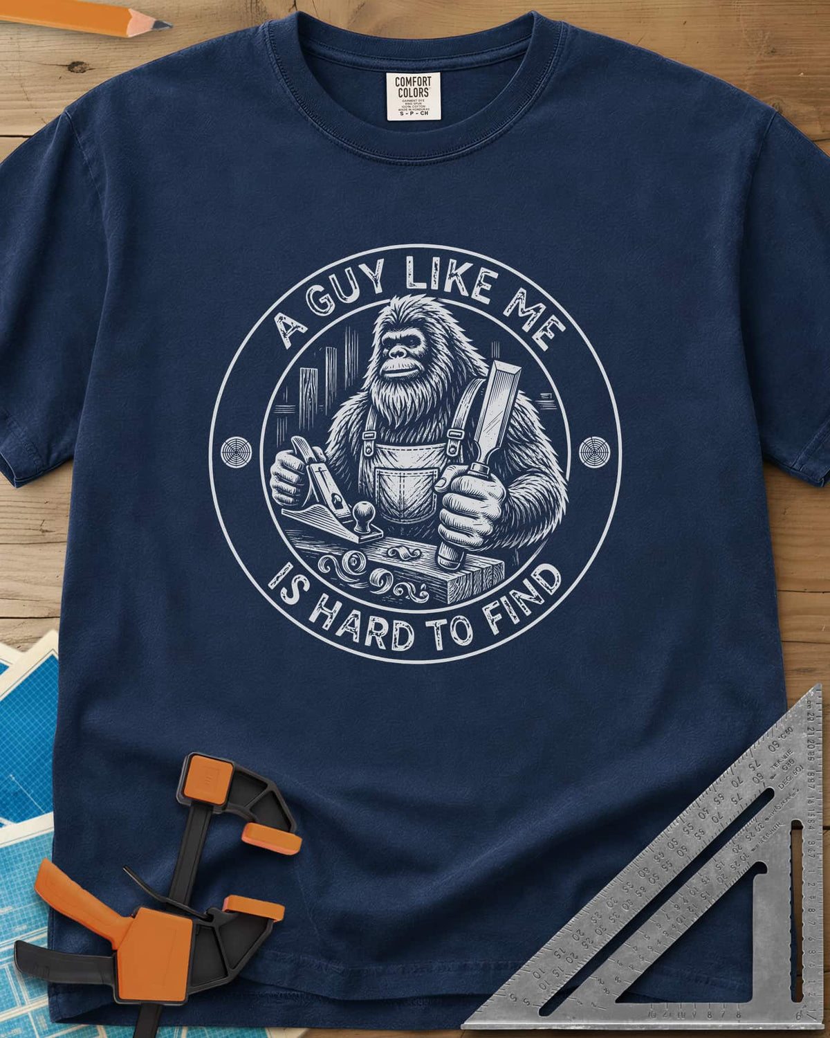 A Guy Like Me Is Hard To Find Woodworking heavyweight tee in Navy, Bigfoot in overalls with a hand plane and chisel inside a