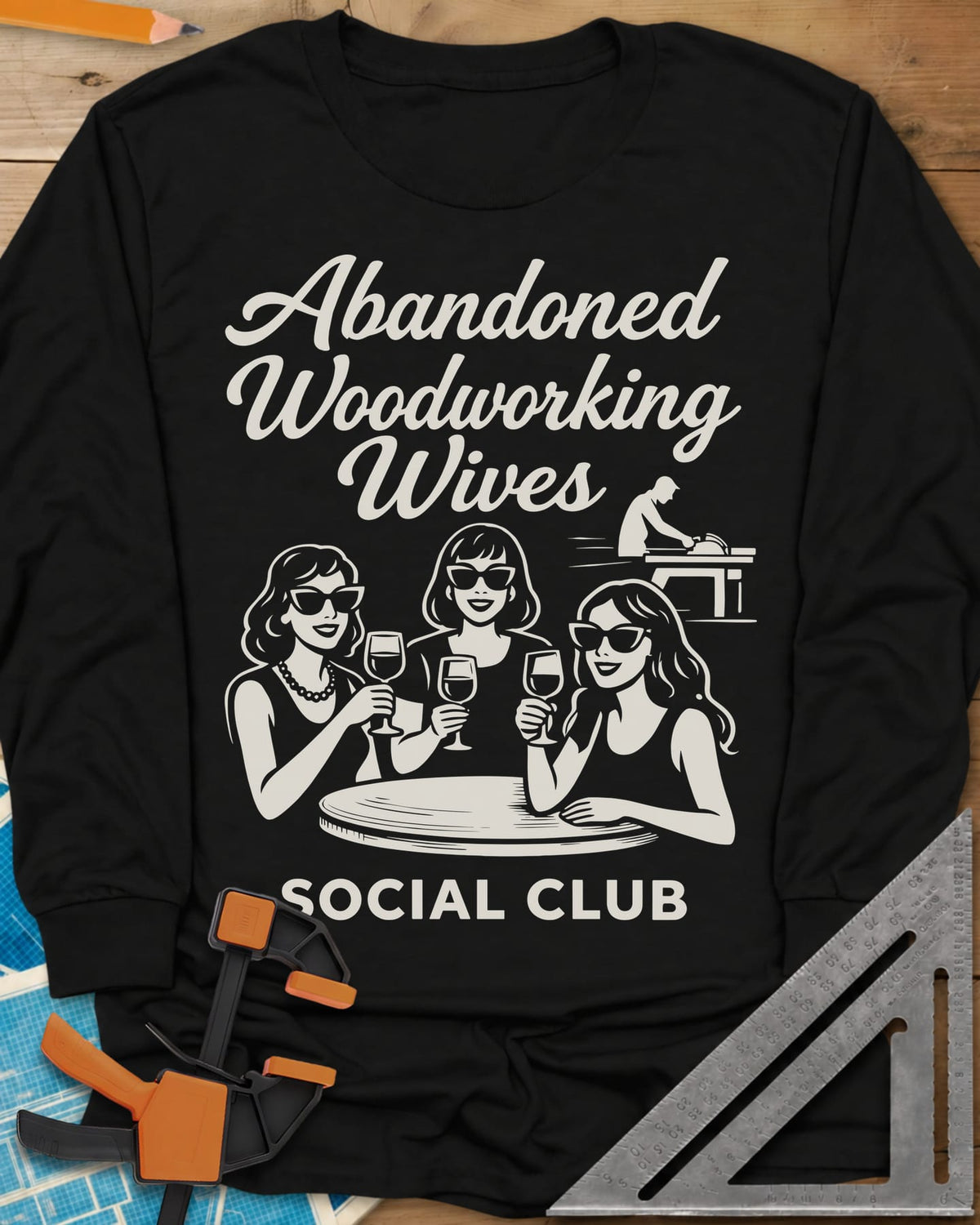 Abandoned Woodworking Wives long sleeve shirt in Black, three women in sunglasses with wine, a man at a table saw behind