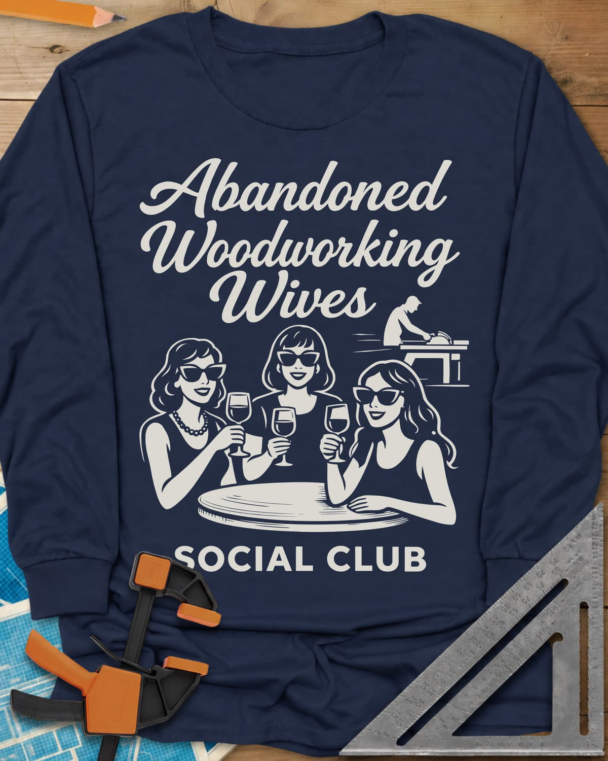 Abandoned Woodworking Wives long sleeve shirt in Navy, three women in sunglasses with wine, a man at a table saw behind