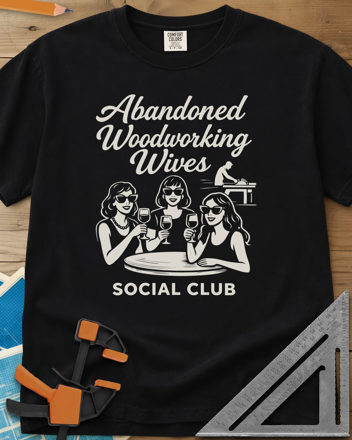 Abandoned Woodworking Wives heavyweight tee in Black, three women in sunglasses with wine, a man at a table saw behind