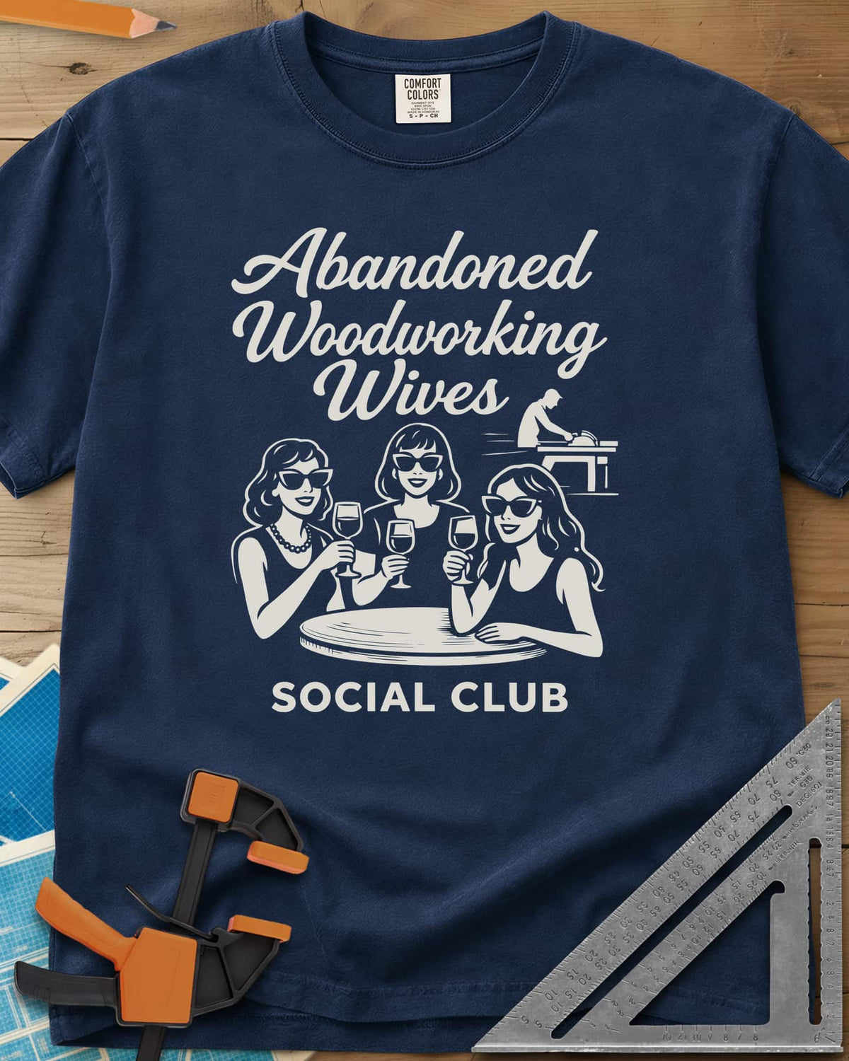 Abandoned Woodworking Wives heavyweight tee in Navy, three women in sunglasses with wine, a man at a table saw behind