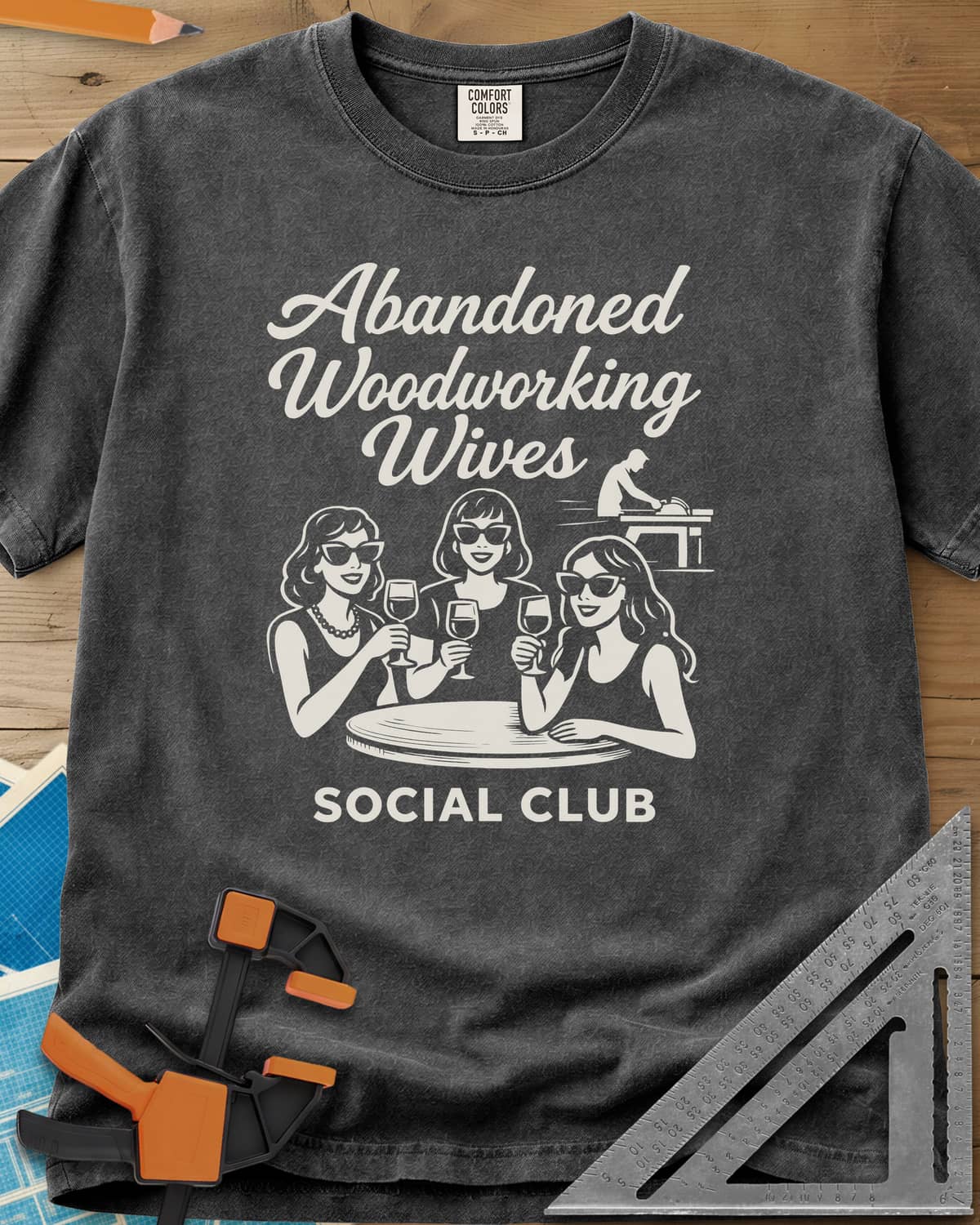 Abandoned Woodworking Wives heavyweight tee in Pepper, three women in sunglasses with wine, a man at a table saw behind