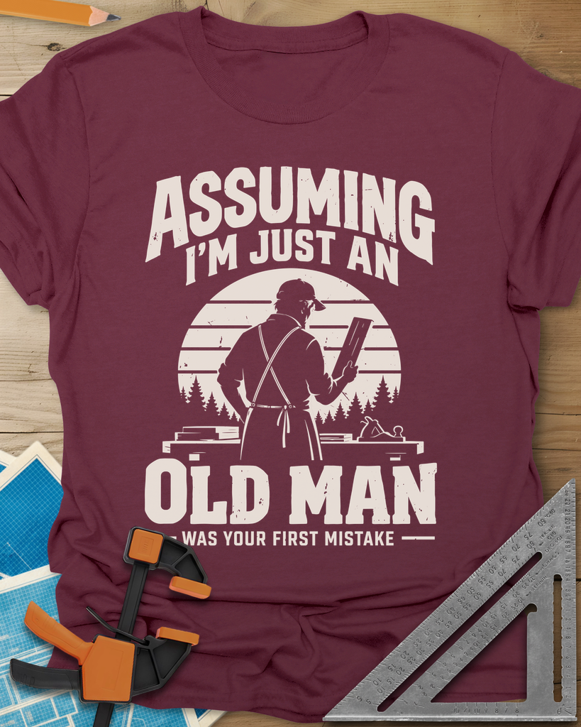 Old Man Mistake t-shirt in Maroon, a woodworker in an apron holding a board before a striped sunset