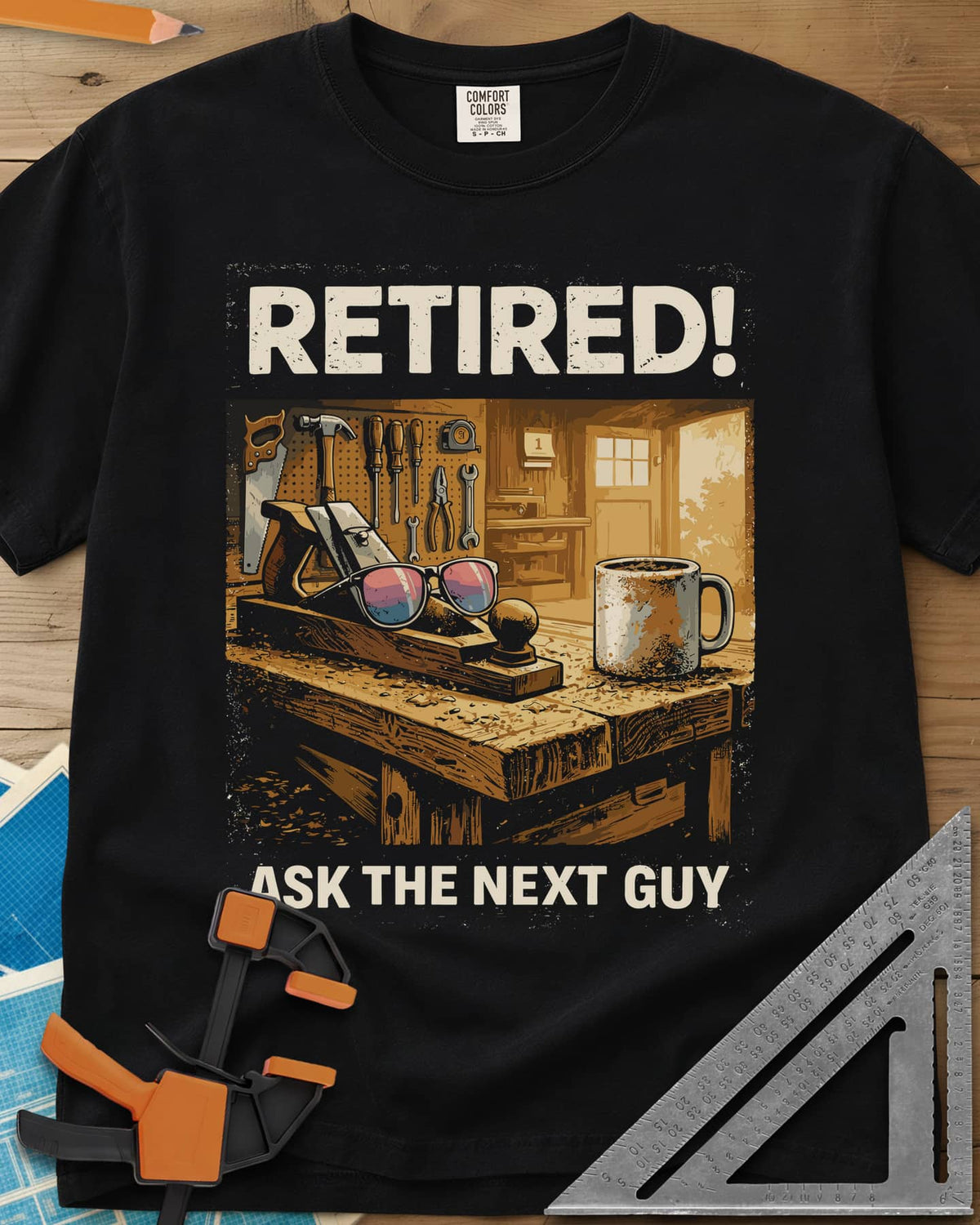 Ask The Next Guy heavyweight tee in Black, a sunlit workbench with a hand plane, sunglasses and a coffee mug