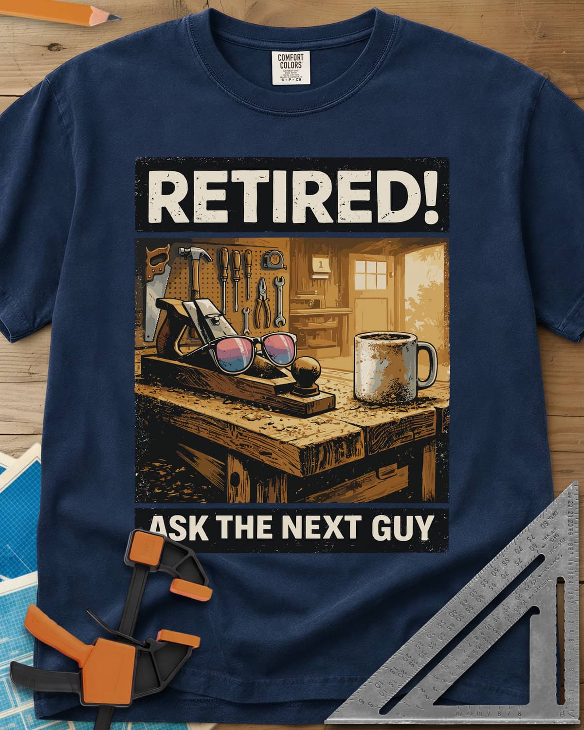 Ask The Next Guy heavyweight tee in Navy, a sunlit workbench with a hand plane, sunglasses and a coffee mug