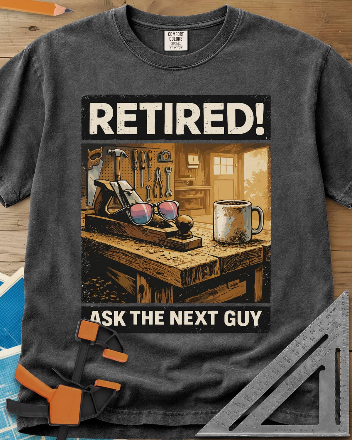 Ask The Next Guy heavyweight tee in Pepper, a sunlit workbench with a hand plane, sunglasses and a coffee mug