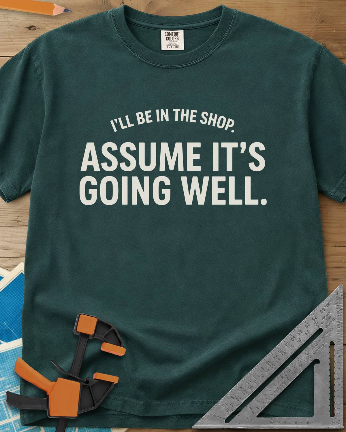 Assume It's Going Well heavyweight tee in Blue Spruce, bold two-line lettering with a small arched line above