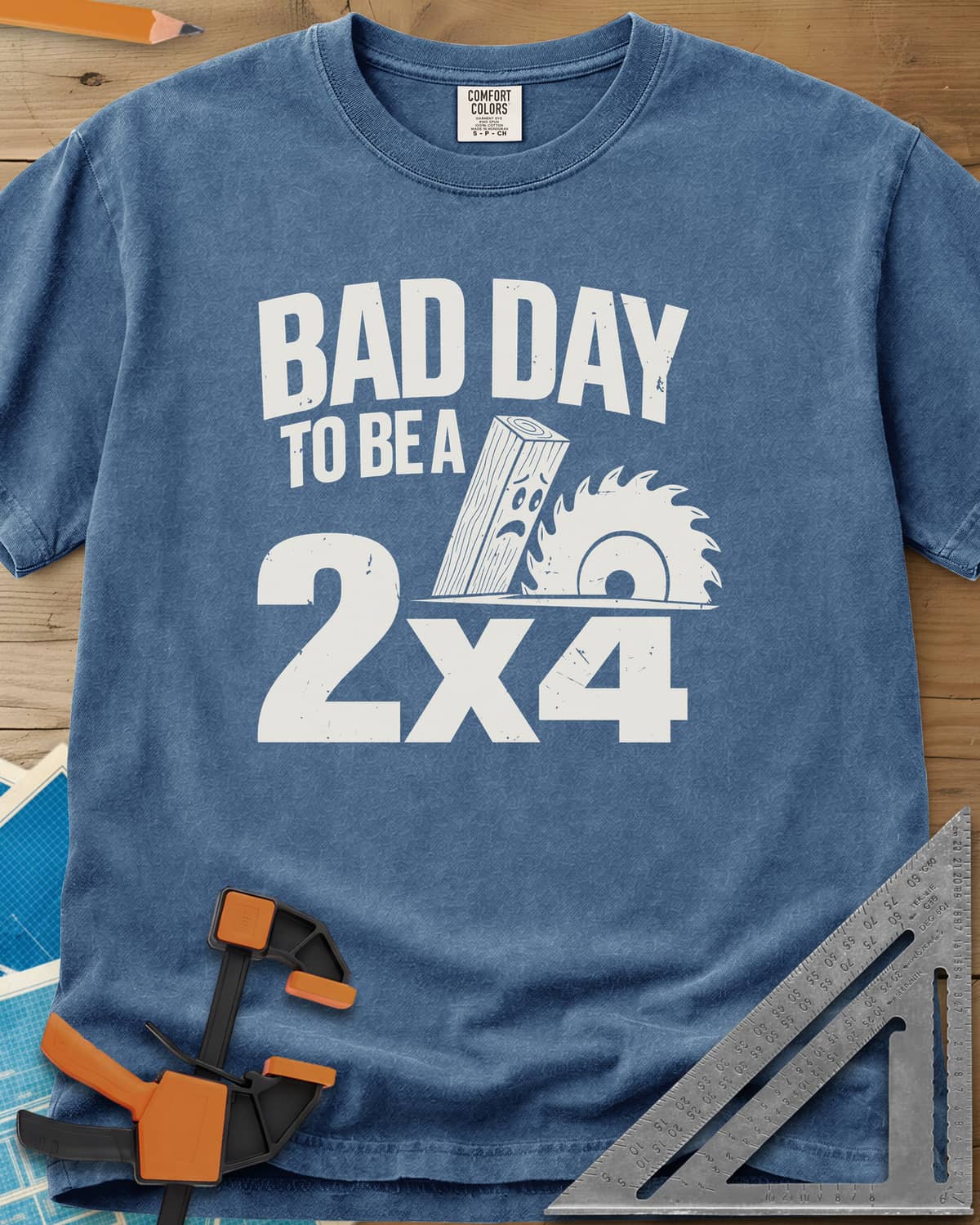 Bad Day 2x4 heavyweight tee in Blue Jean, a 2x4 board with a worried face beside a circular saw blade