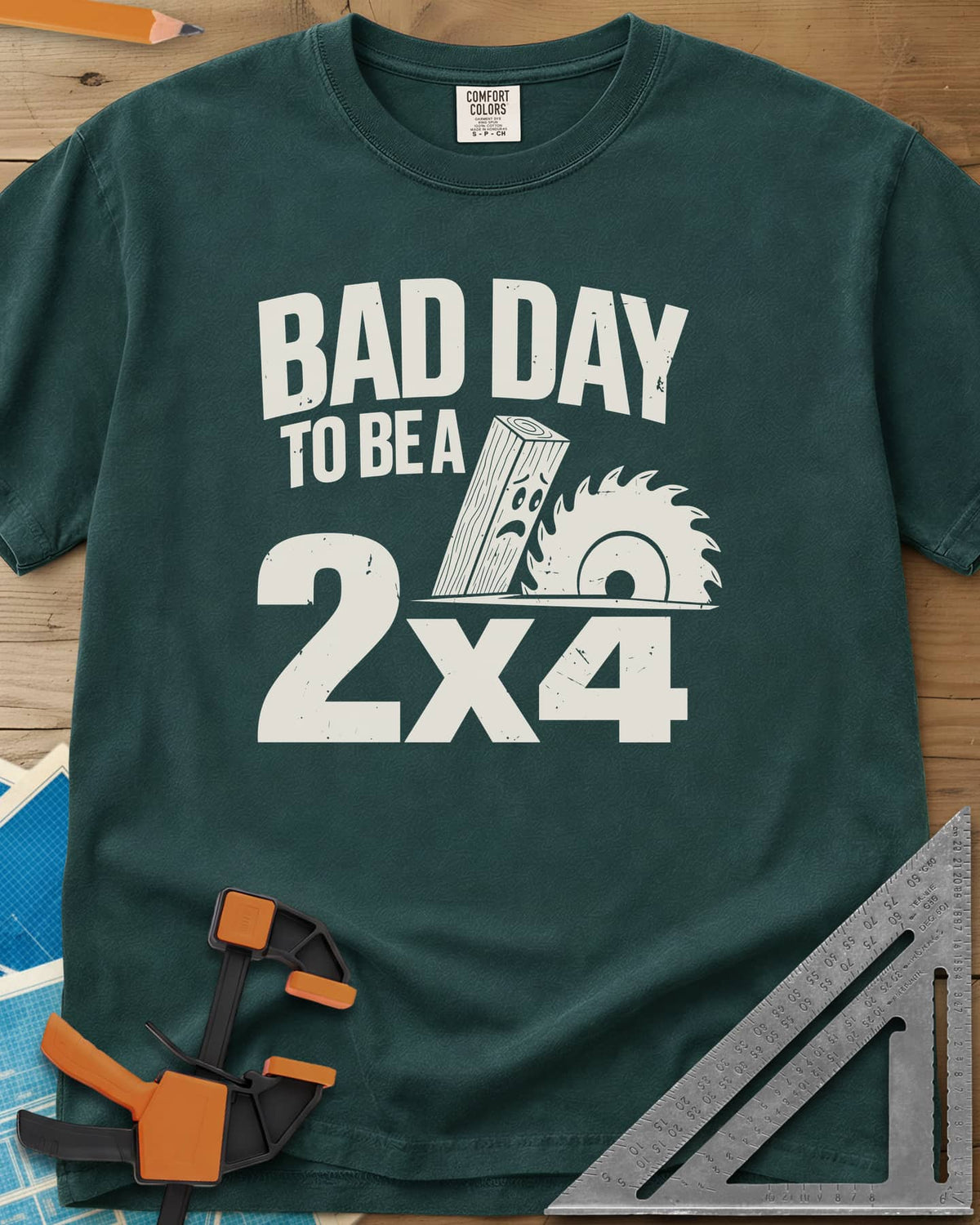 Bad Day 2x4 heavyweight tee in Blue Spruce, a 2x4 board with a worried face beside a circular saw blade