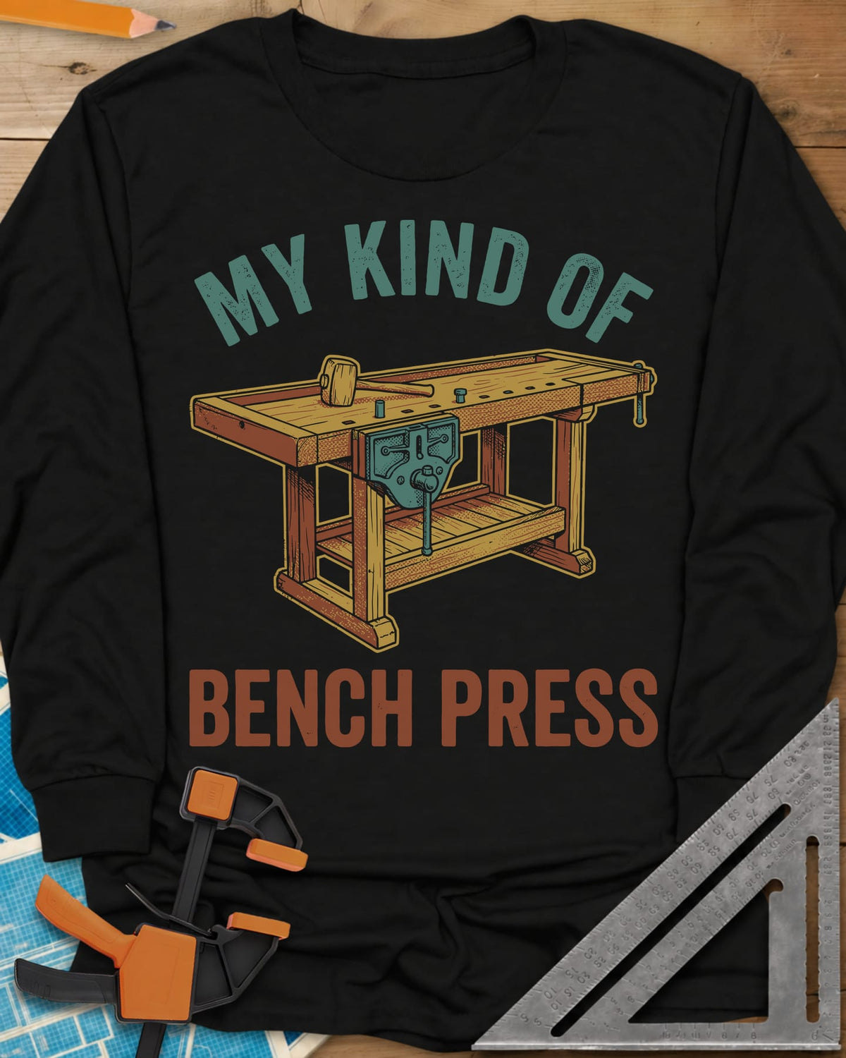 Bench Press long sleeve shirt in Black, a wooden workbench with a vise and mallet between the two lines