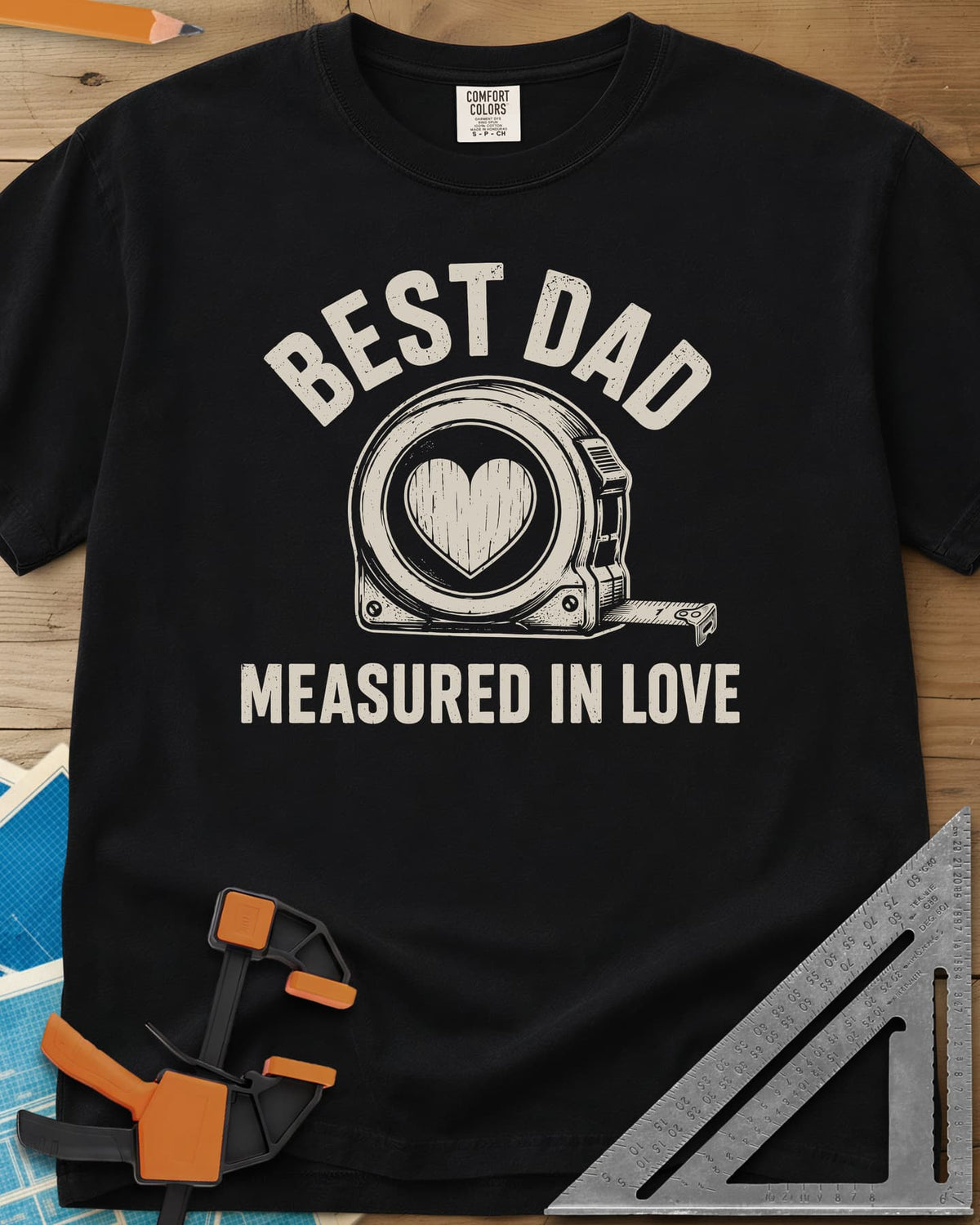 Best Dad Measured In Love heavyweight tee in Black, a round tape measure with a wood-grain heart on its face