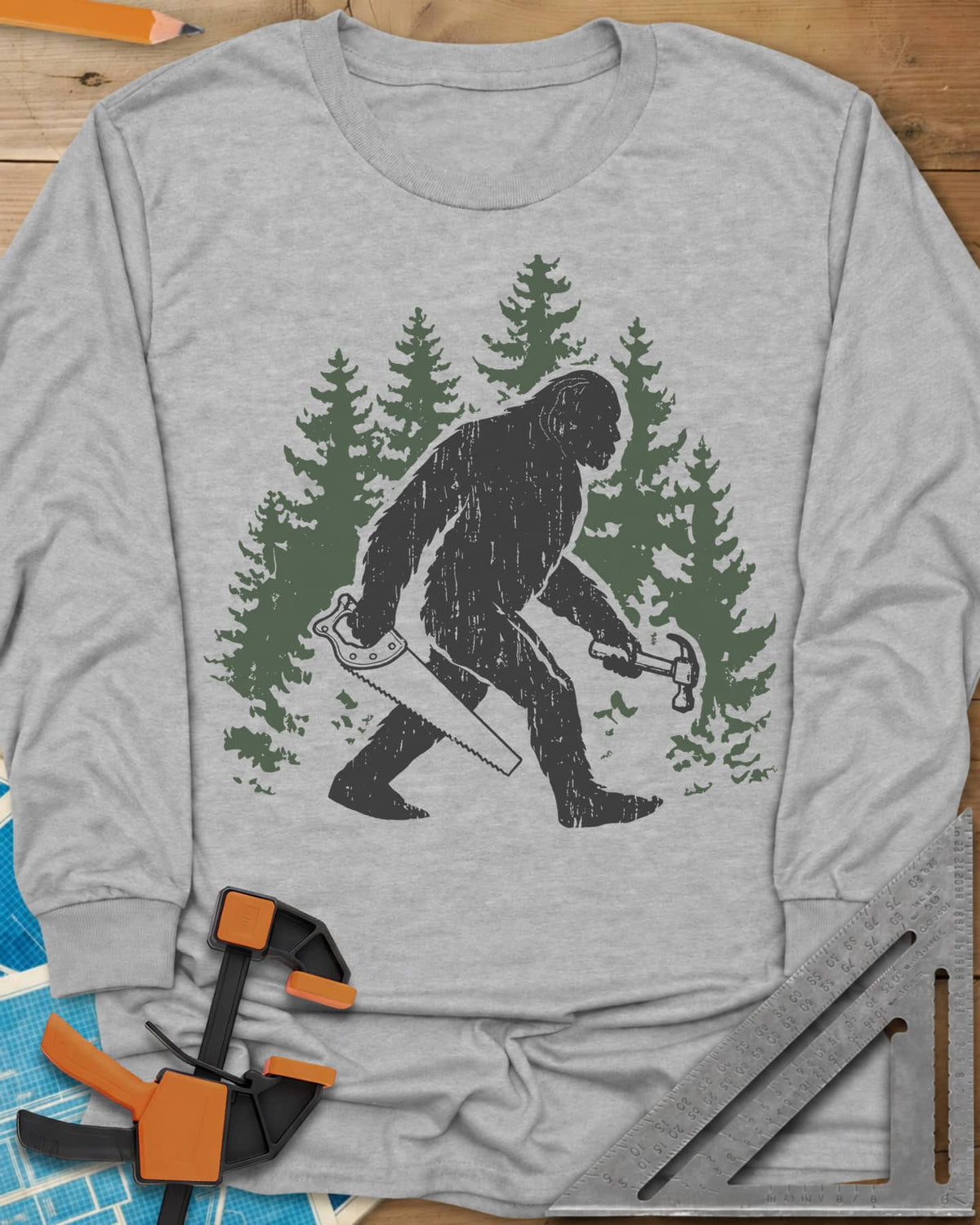Big Foot long sleeve shirt in Sport Grey, Bigfoot walking through pine trees with a hand saw and a hammer