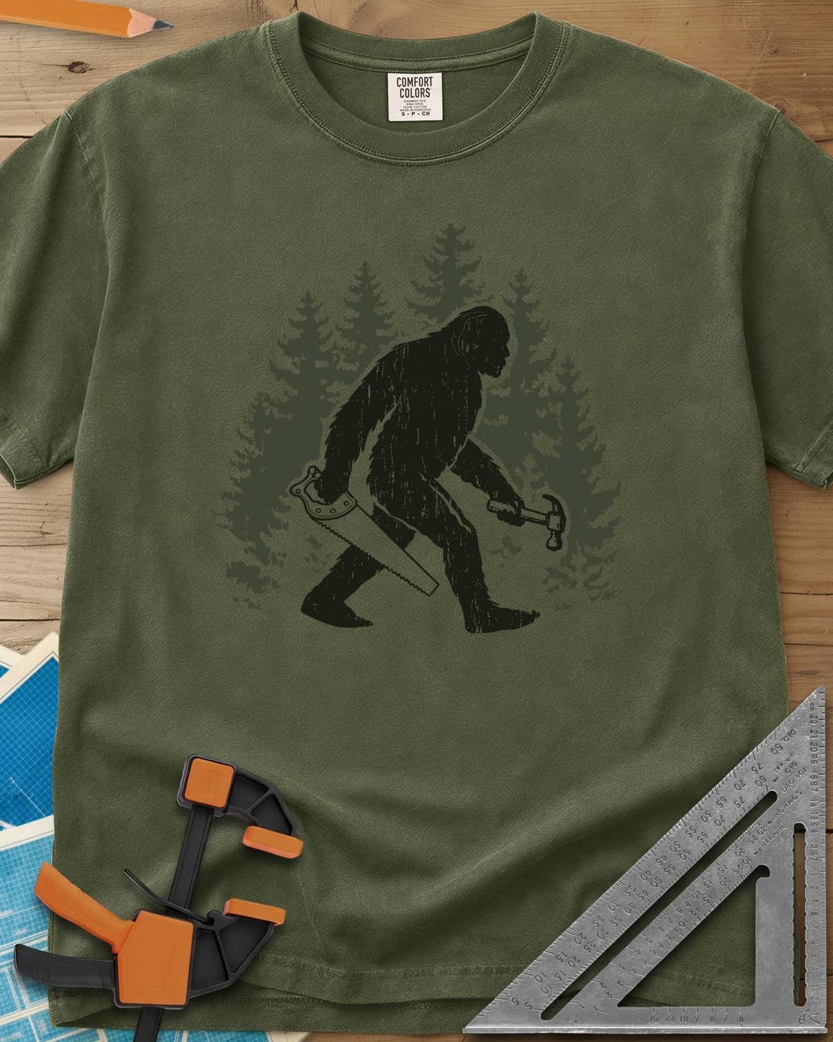Big Foot heavyweight tee in Hemp, Bigfoot walking through pine trees with a hand saw and a hammer