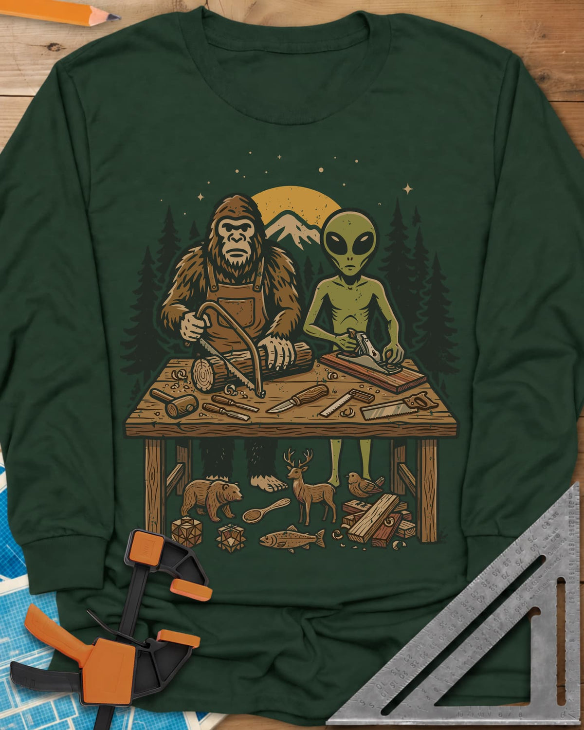 Bigfoot And Alien Woodshop long sleeve shirt in Forest Green, Bigfoot sawing a log and an alien planing a board at one bench