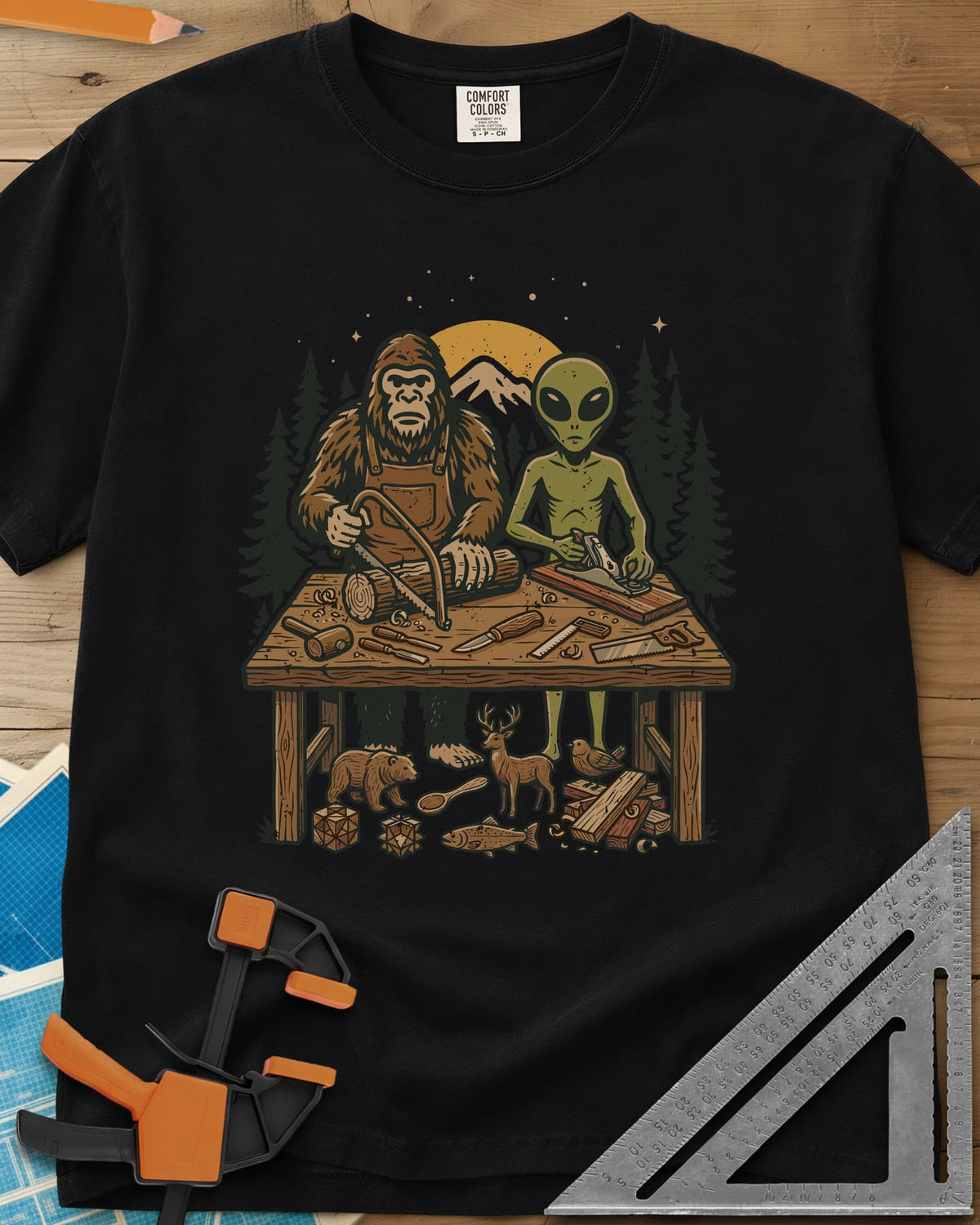 Bigfoot And Alien Woodshop heavyweight tee in Black, Bigfoot sawing a log and an alien planing a board at one bench