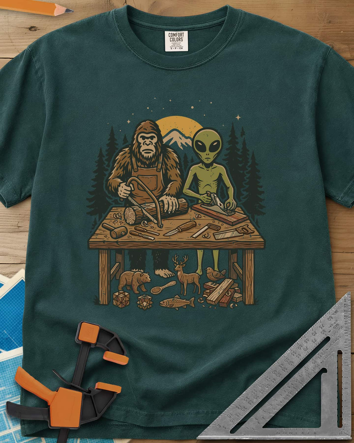 Bigfoot And Alien Woodshop heavyweight tee in Blue Spruce, Bigfoot sawing a log and an alien planing a board at one bench