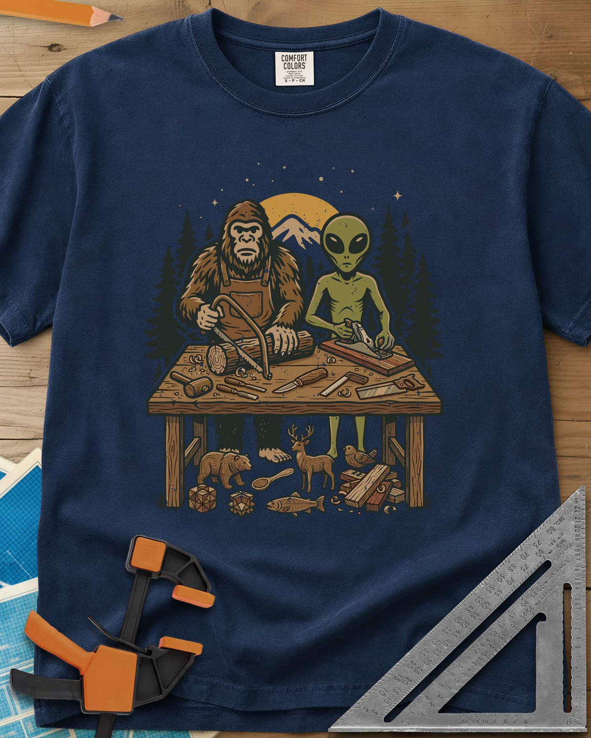 Bigfoot And Alien Woodshop heavyweight tee in Navy, Bigfoot sawing a log and an alien planing a board at one bench