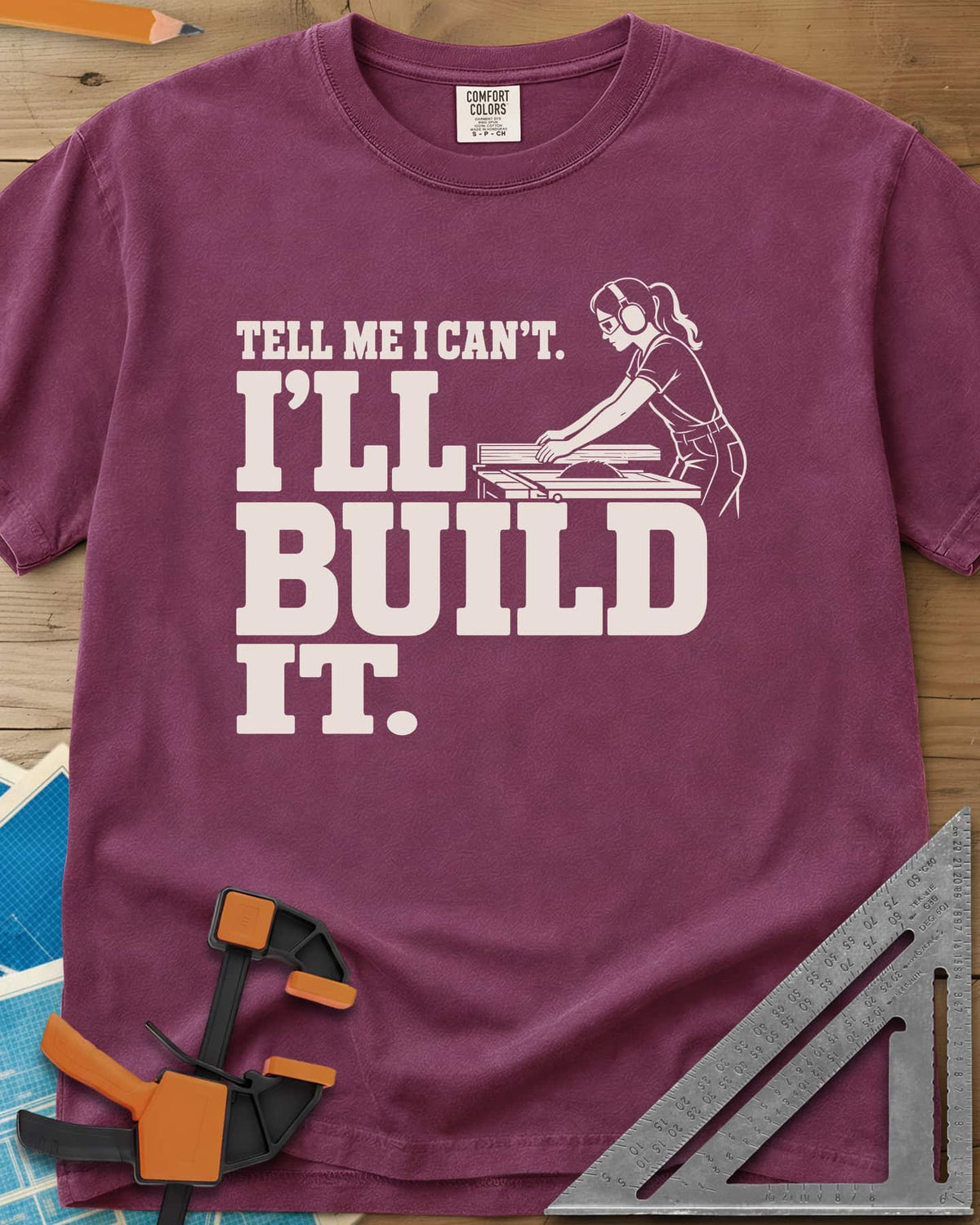 Build It heavyweight tee in Berry, a woman in ear protection and safety glasses at a table saw