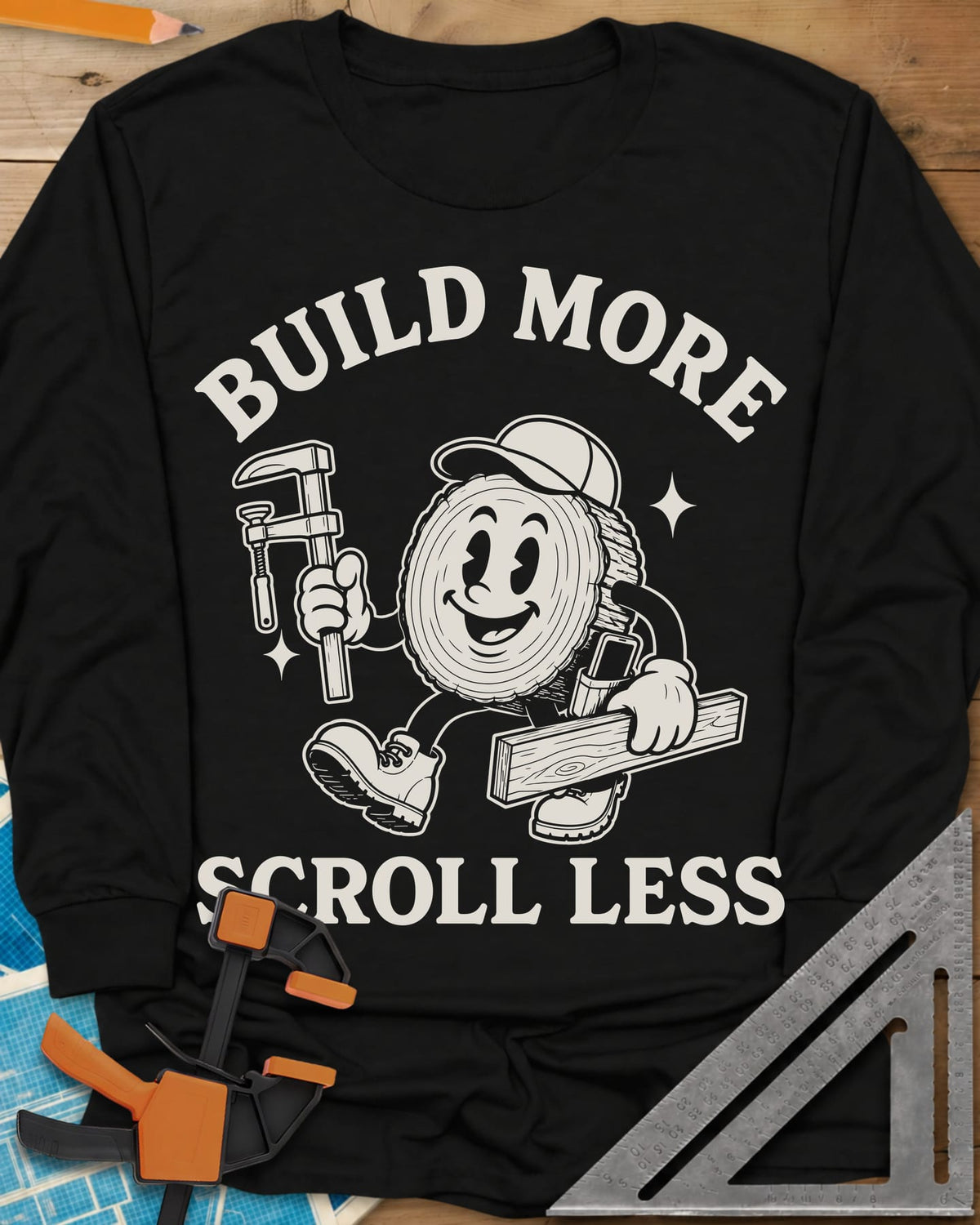 Build More Scroll Less long sleeve shirt in Black, a smiling log-slice mascot in boots carrying a tool and a board