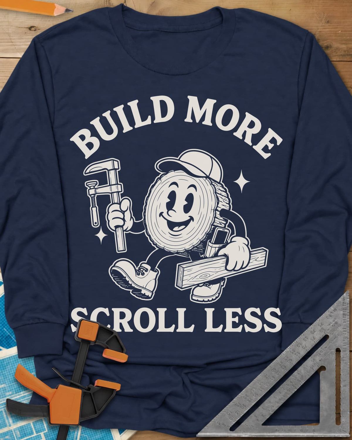 Build More Scroll Less long sleeve shirt in Navy, a smiling log-slice mascot in boots carrying a tool and a board