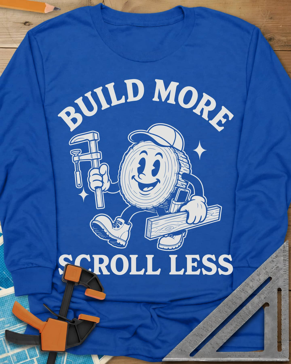 Build More Scroll Less long sleeve shirt in Royal, a smiling log-slice mascot in boots carrying a tool and a board