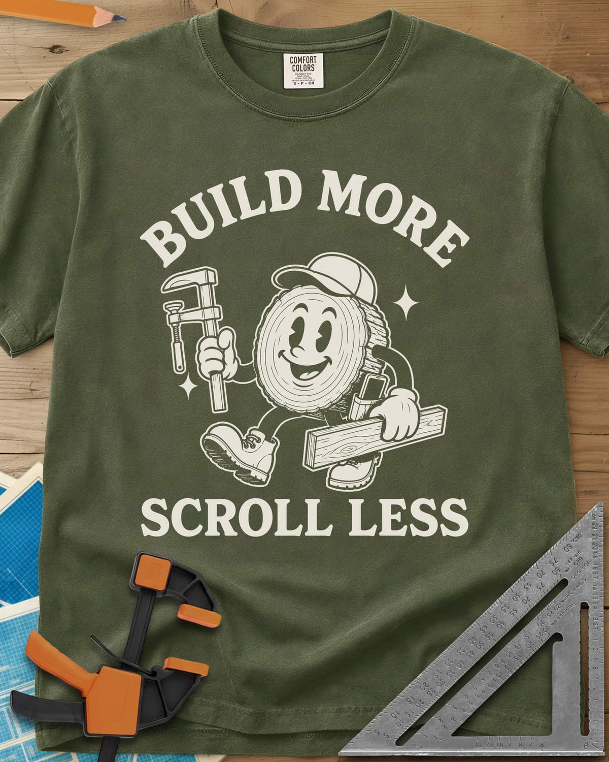 Build More Scroll Less heavyweight tee in Hemp, a smiling log-slice mascot in boots carrying a tool and a board