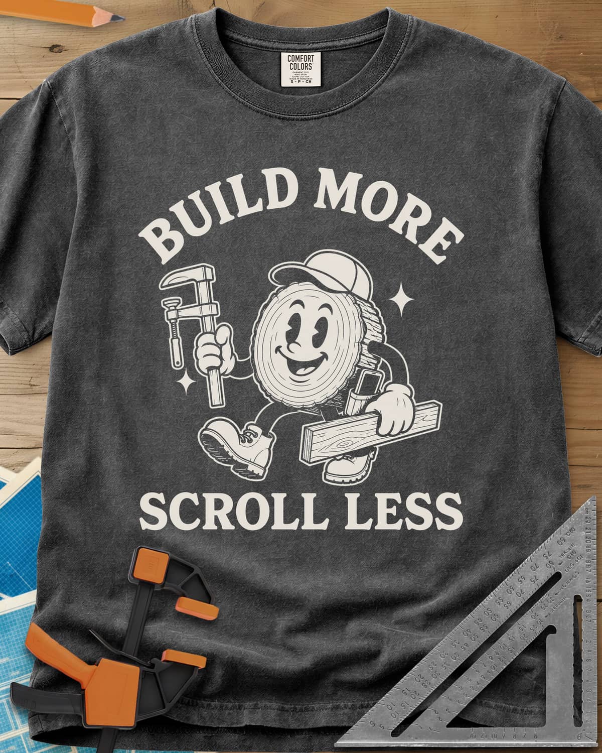 Build More Scroll Less heavyweight tee in Pepper, a smiling log-slice mascot in boots carrying a tool and a board