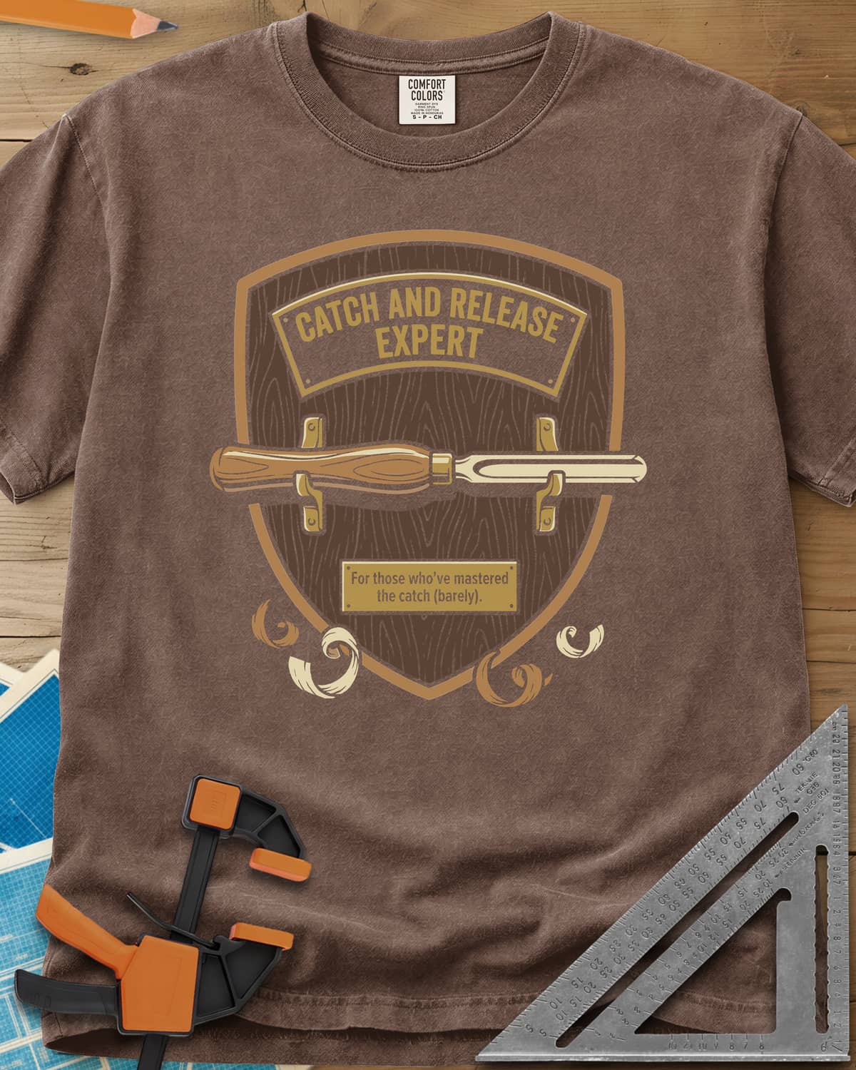 Catch and Release heavyweight tee in Espresso, a wooden shield plaque with a turning gouge and brass nameplate