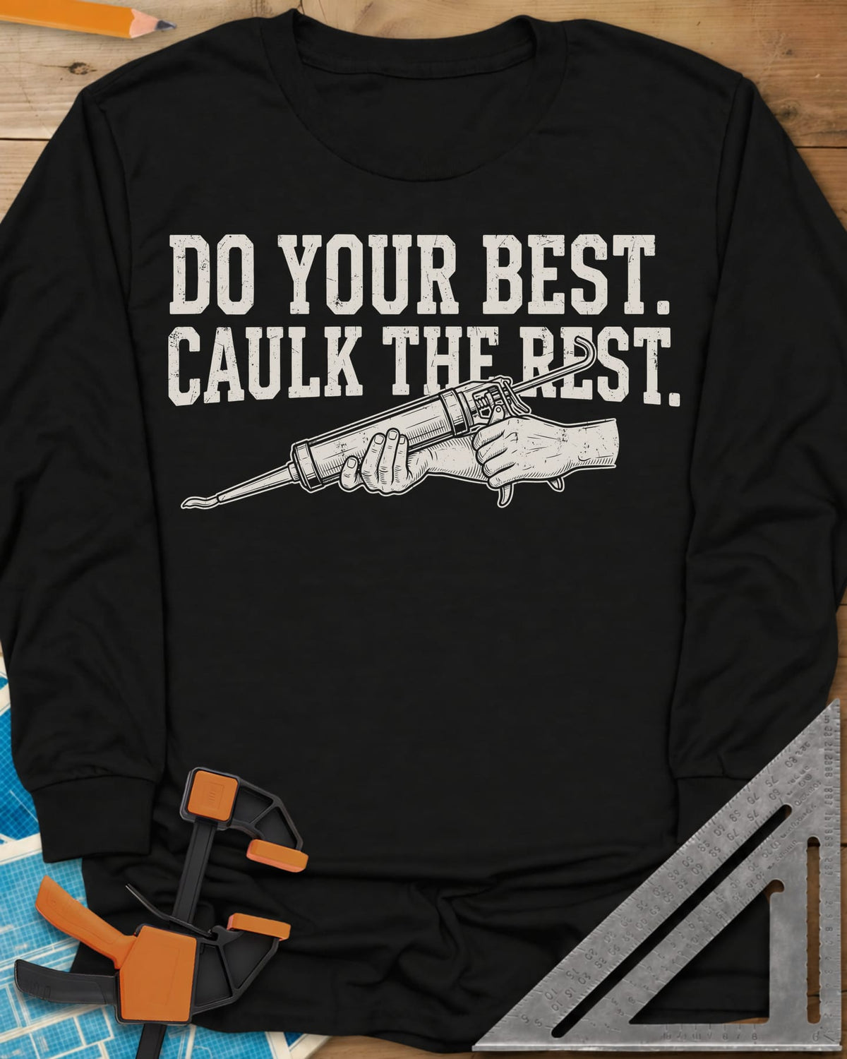 Caulk The Rest long sleeve shirt in Black, hands working a caulk gun under two lines of block lettering