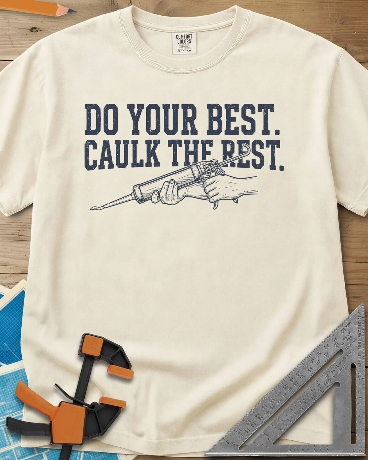 Caulk The Rest heavyweight tee in Ivory, hands working a caulk gun under two lines of block lettering