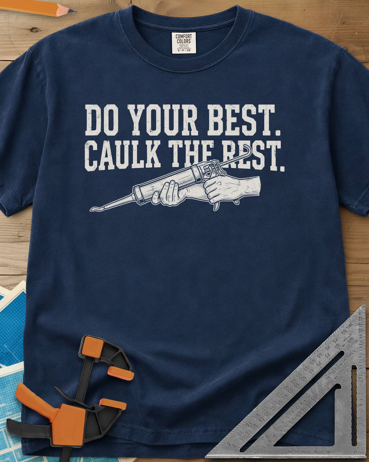 Caulk The Rest heavyweight tee in Navy, hands working a caulk gun under two lines of block lettering