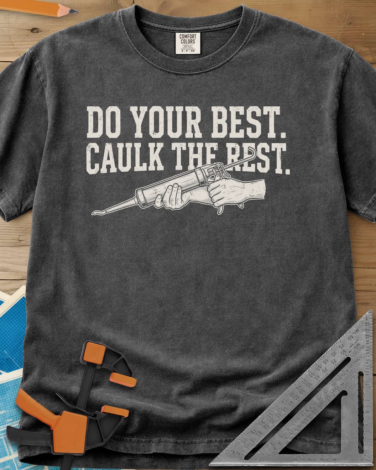 Caulk The Rest heavyweight tee in Pepper, hands working a caulk gun under two lines of block lettering