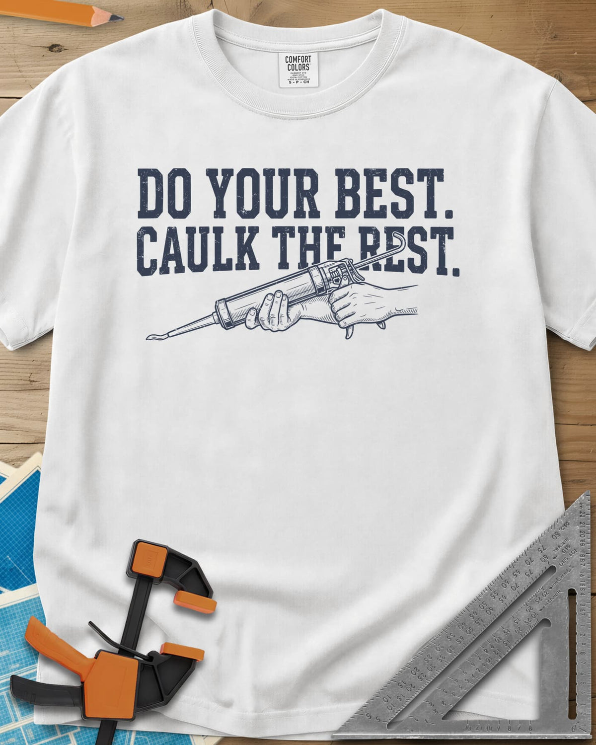 Caulk The Rest heavyweight tee in White, hands working a caulk gun under two lines of block lettering
