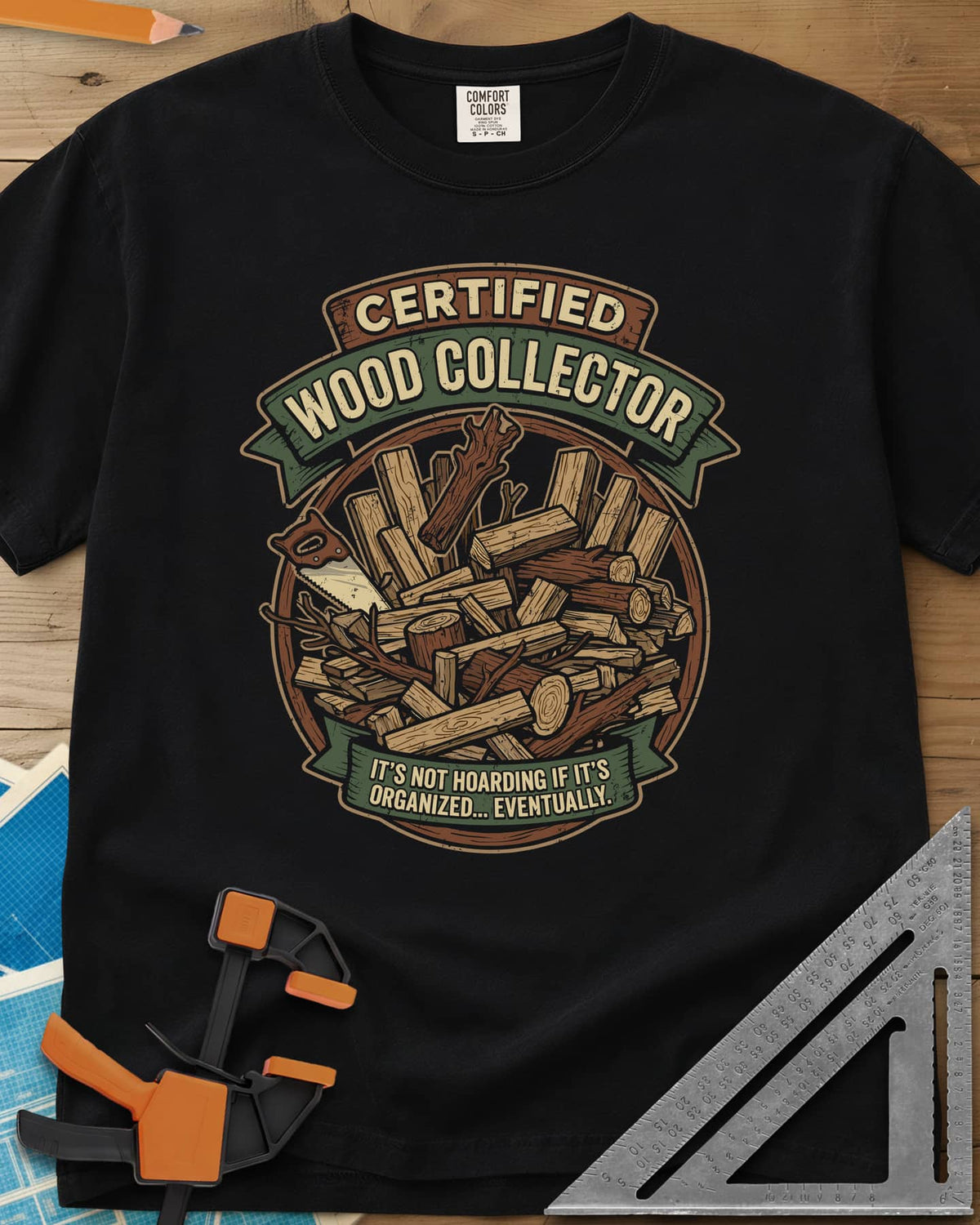 Certified Wood Collector heavyweight tee in Black, ribbon banners over a heap of logs, offcuts and a handsaw