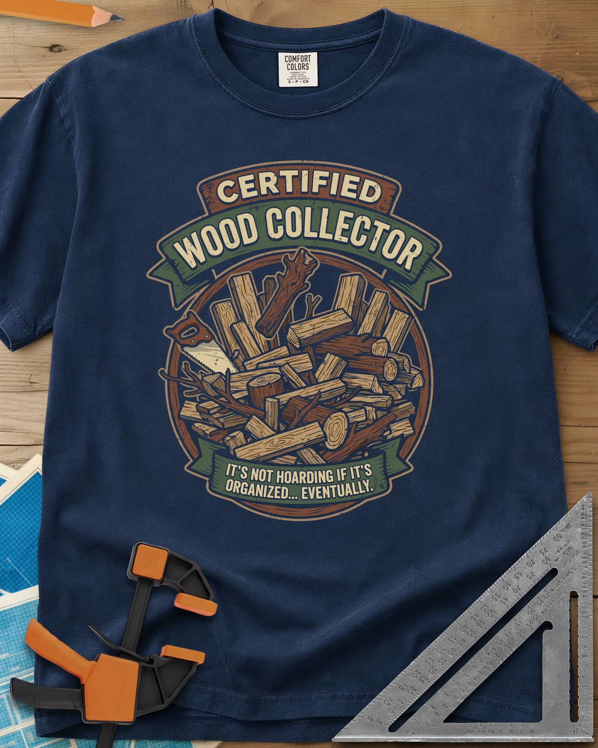 Certified Wood Collector heavyweight tee in Navy, ribbon banners over a heap of logs, offcuts and a handsaw