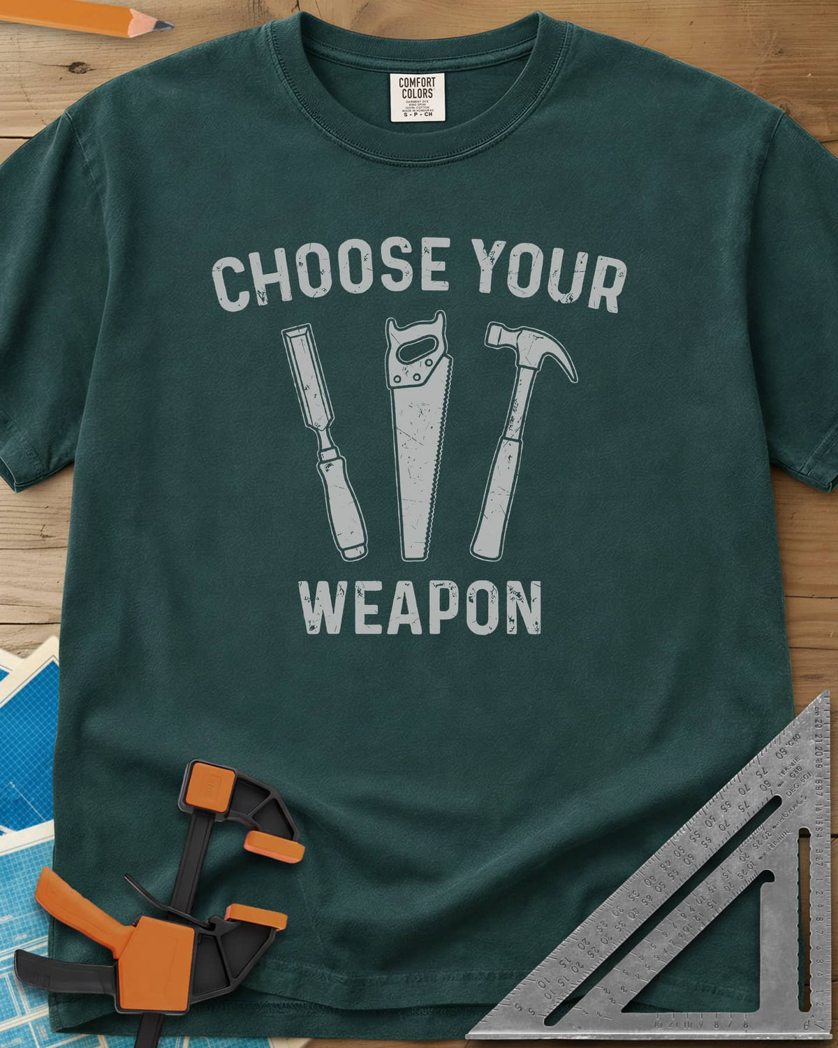 Choose Your Weapon heavyweight tee in Blue Spruce, a chisel, a handsaw and a claw hammer standing in a row