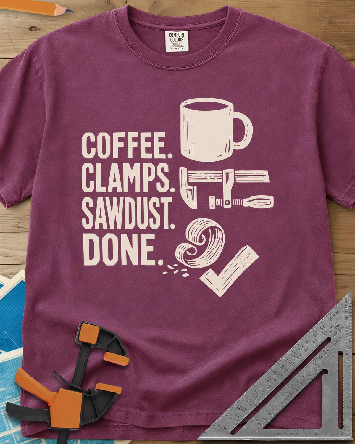 Coffee Clamps heavyweight tee in Berry, a mug, a bar clamp, a wood shaving curl and a check mark