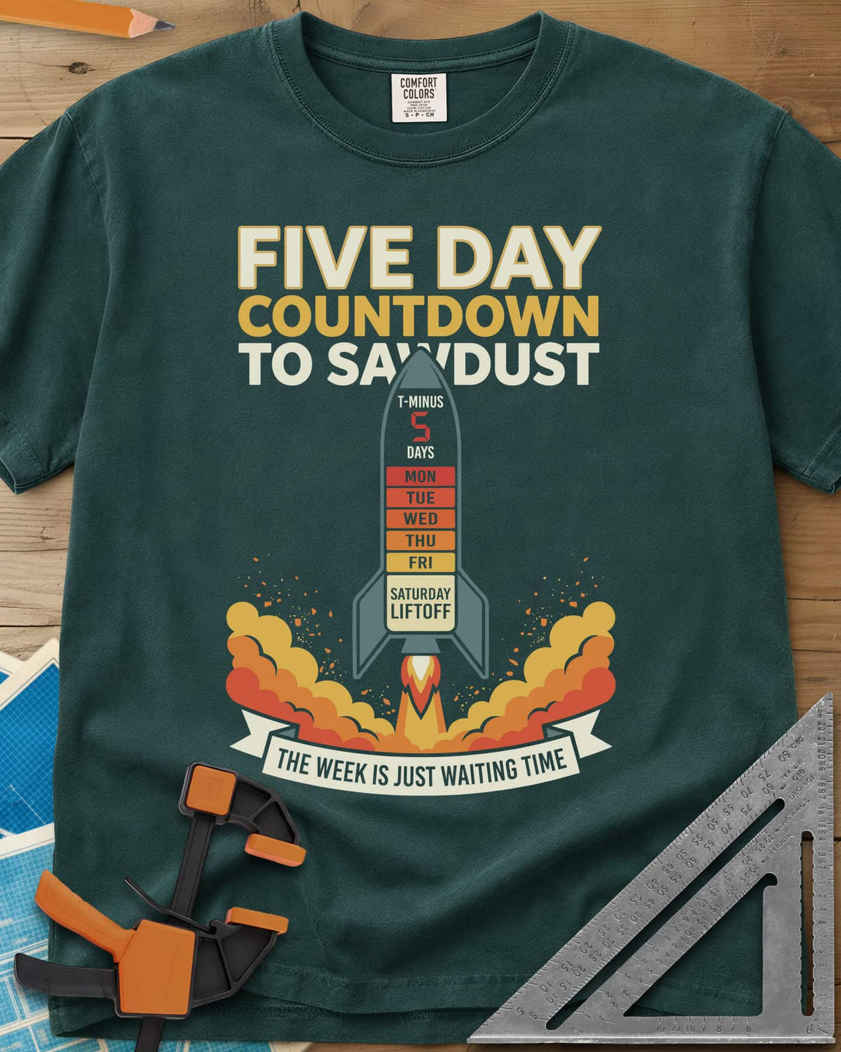 Countdown to Sawdust heavyweight tee in Blue Spruce, a rocket with a Monday-to-Saturday countdown on its hull