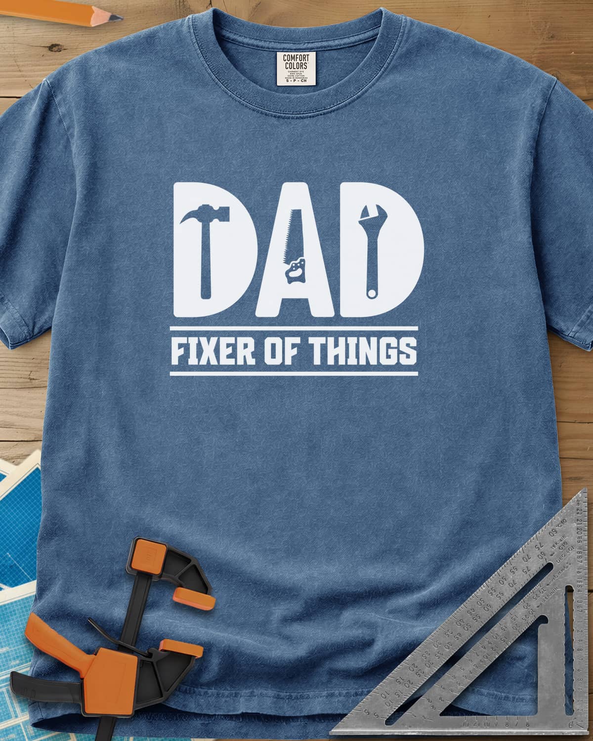 Dad, Fixer of All Things heavyweight tee in Blue Jean, big letters spelling DAD with a hammer, saw and wrench cut in