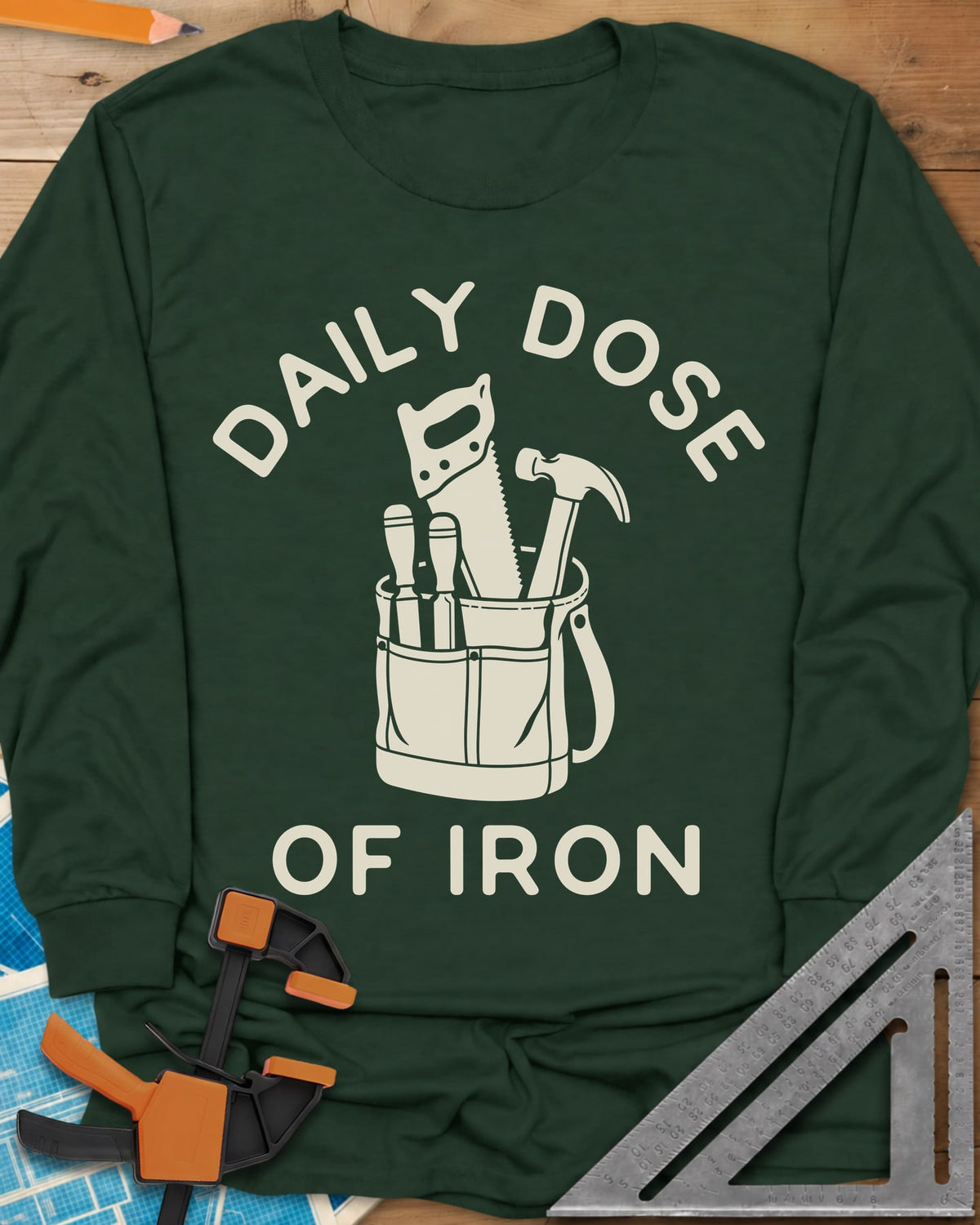 Daily Dose long sleeve shirt in Forest Green, a canvas tool bag holding a handsaw, hammer and two chisels