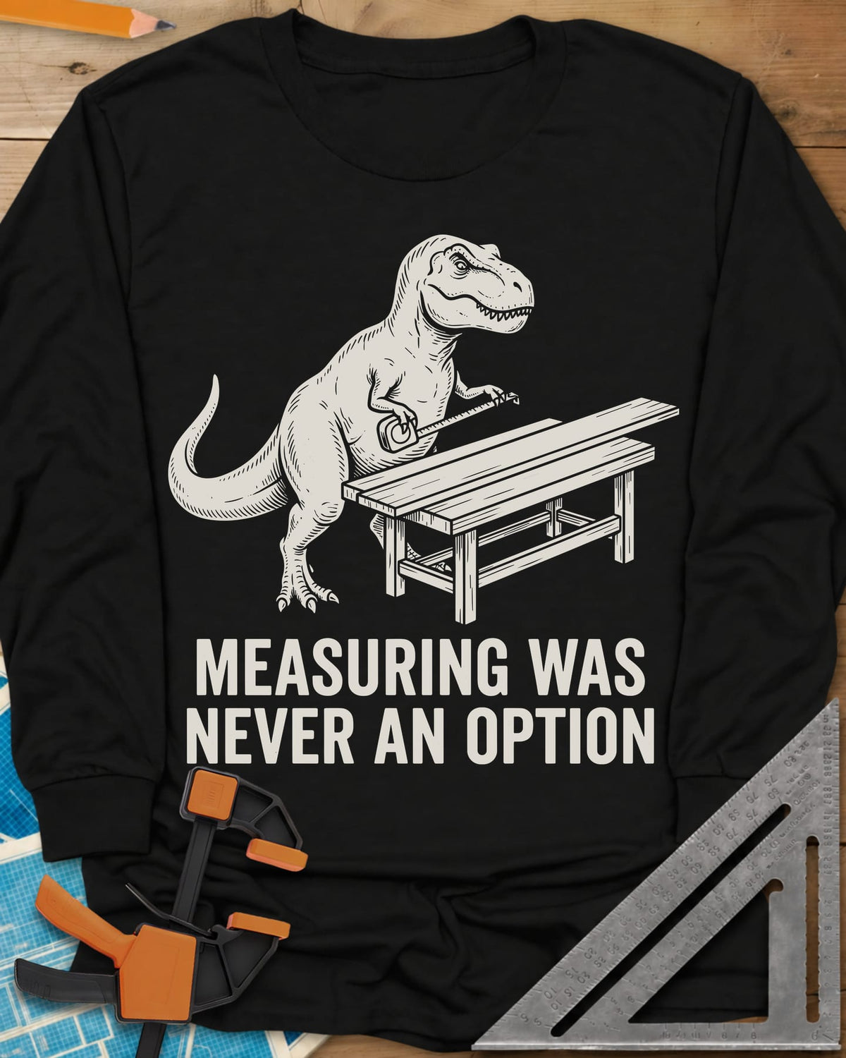 Dino Measuring long sleeve shirt in Black, a T. rex with a tape measure beside a plank workbench