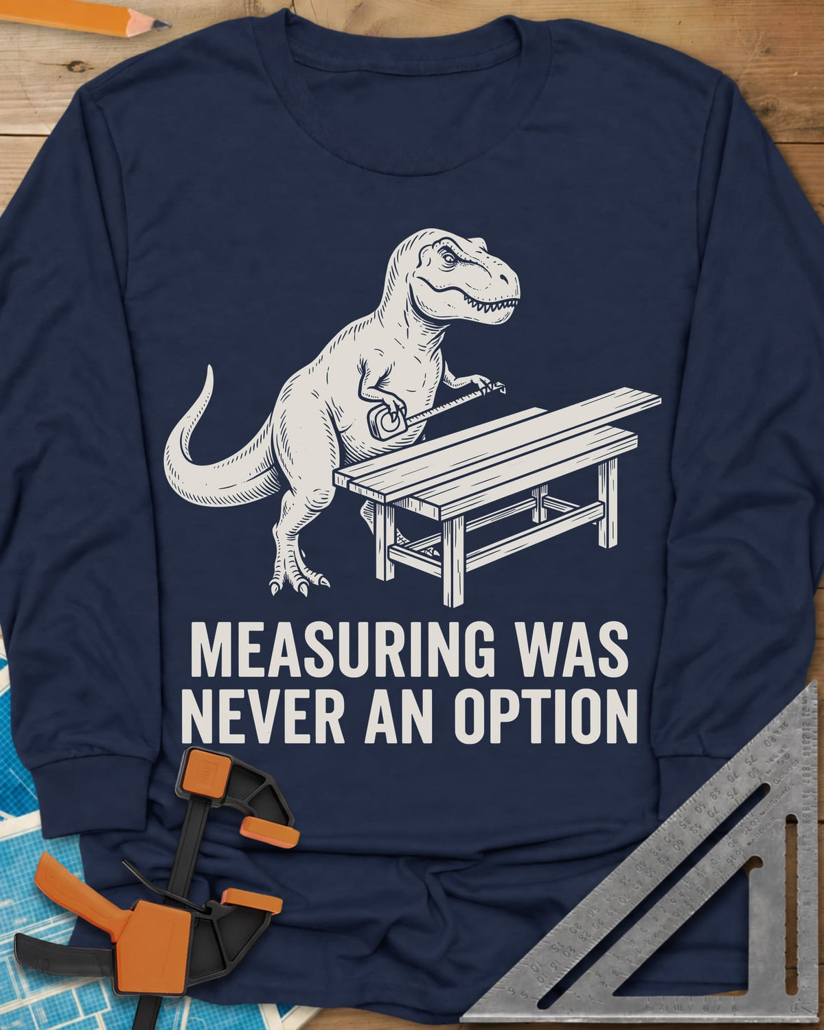 Dino Measuring long sleeve shirt in Navy, a T. rex with a tape measure beside a plank workbench