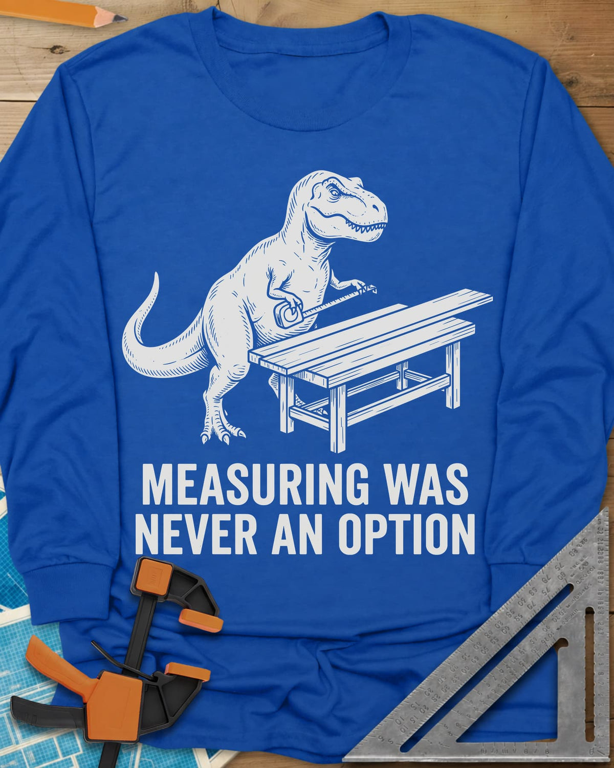 Dino Measuring long sleeve shirt in Royal, a T. rex with a tape measure beside a plank workbench