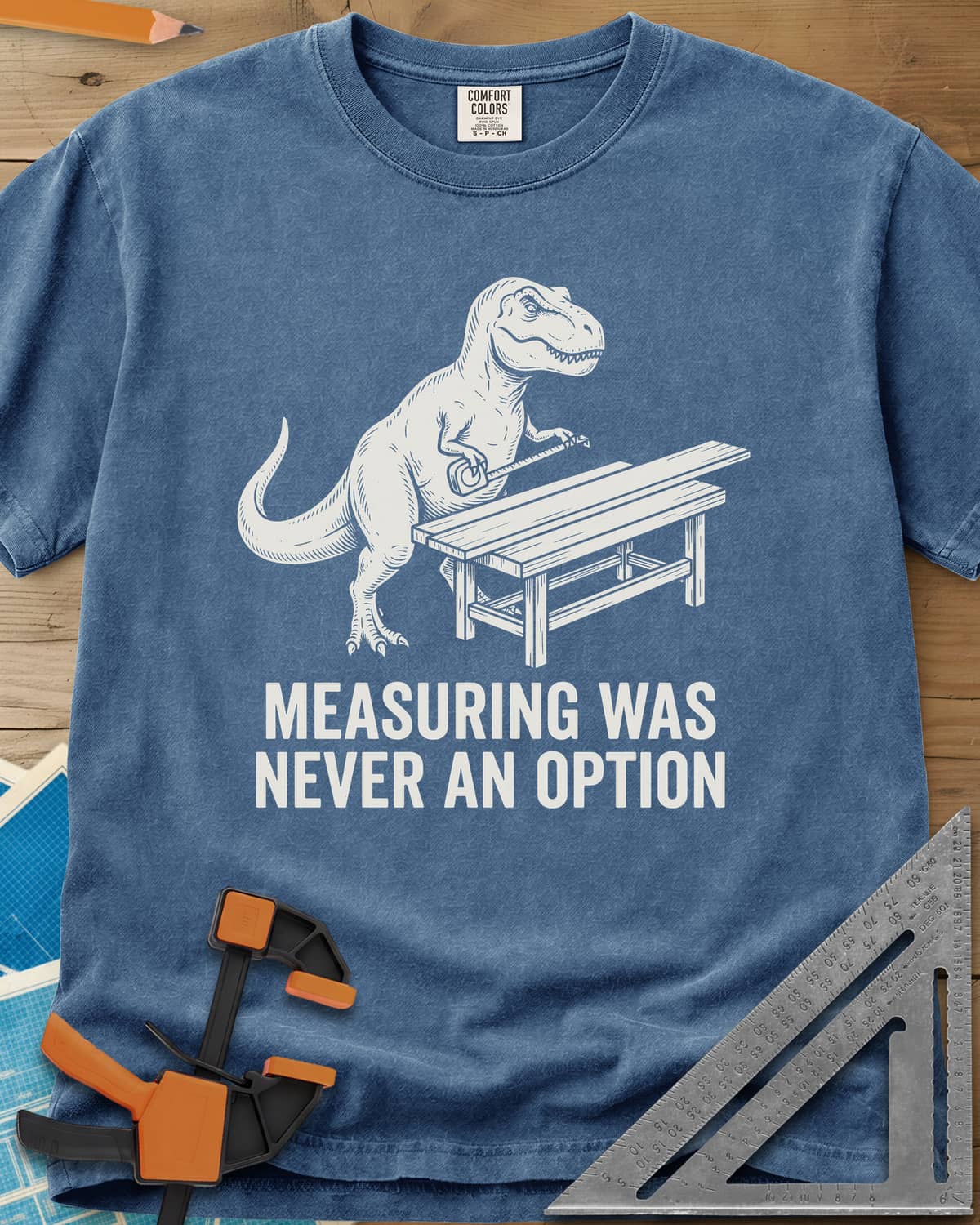 Dino Measuring heavyweight tee in Blue Jean, a T. rex with a tape measure beside a plank workbench