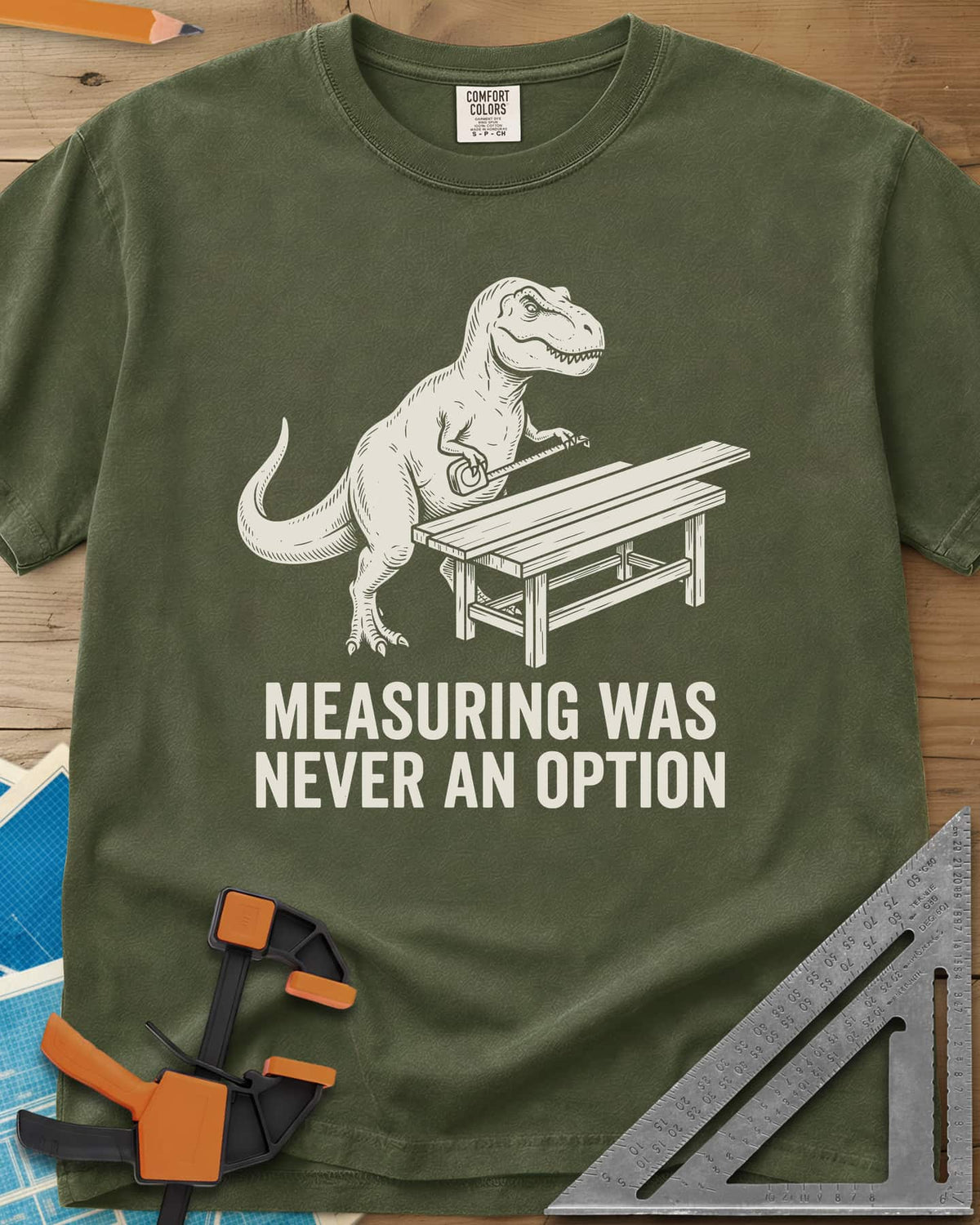 Dino Measuring heavyweight tee in Hemp, a T. rex with a tape measure beside a plank workbench