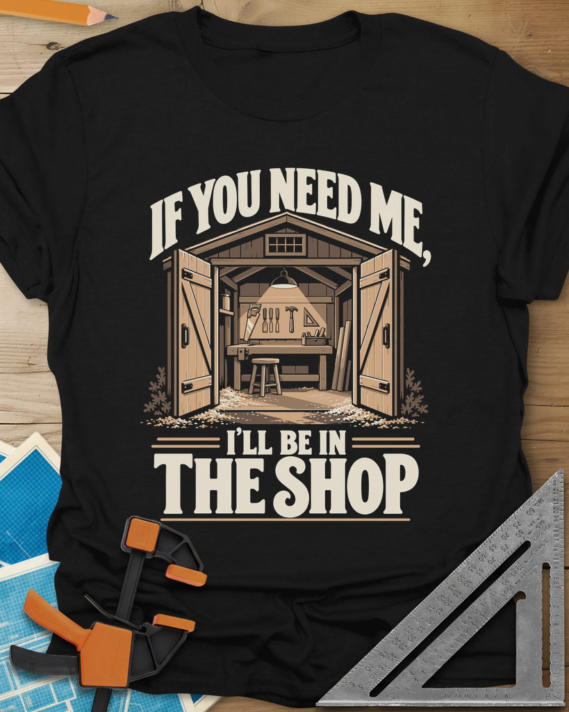 In The Shop t-shirt in Black, a small open workshop with a hanging lamp, bench and wall tools